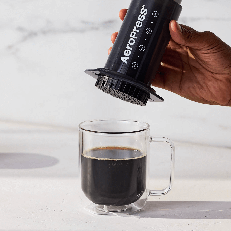 AeroPress brewer held above a glass mug of dark coffee