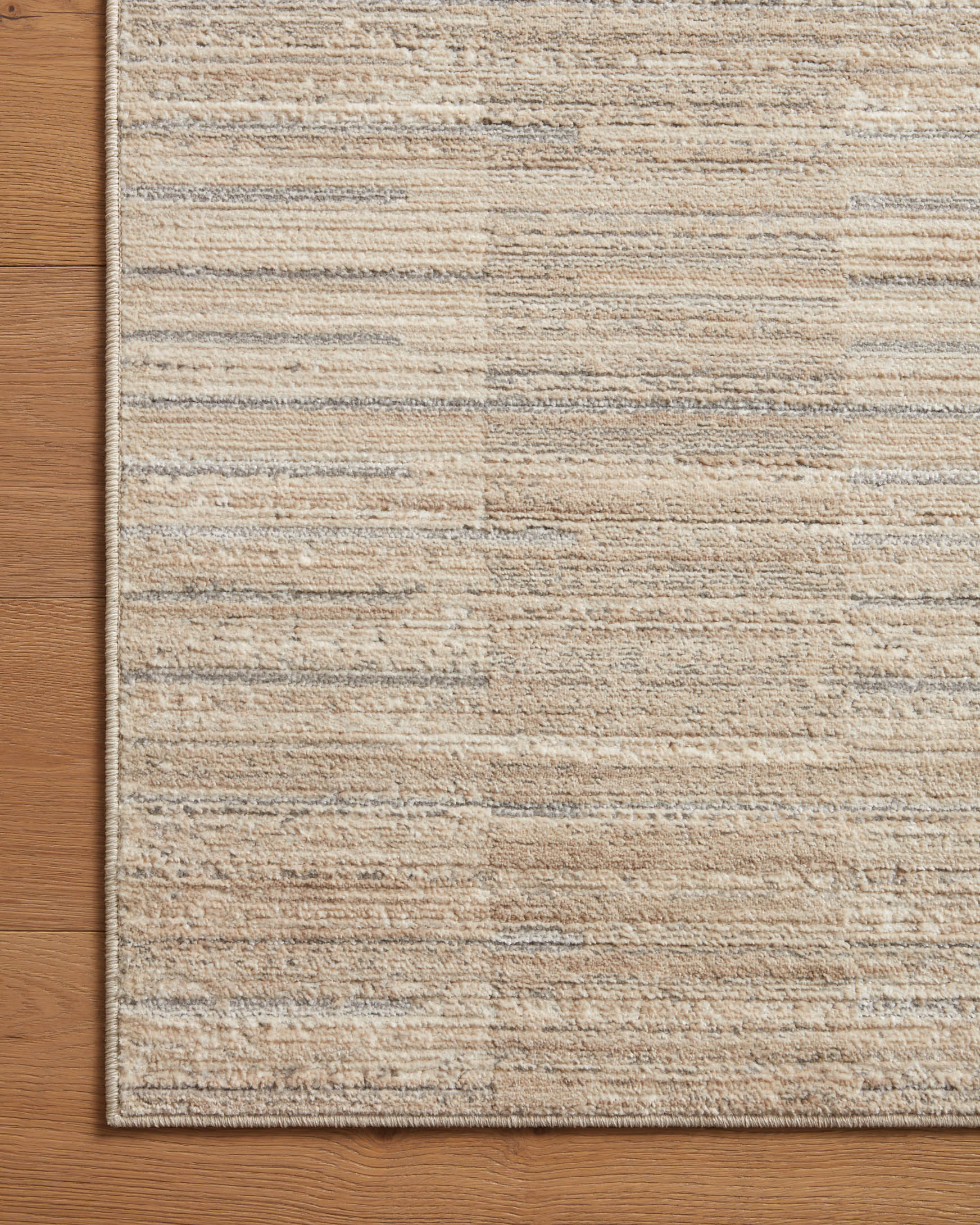 Natural and pebble area rug with textured linear lines and stitched border edge