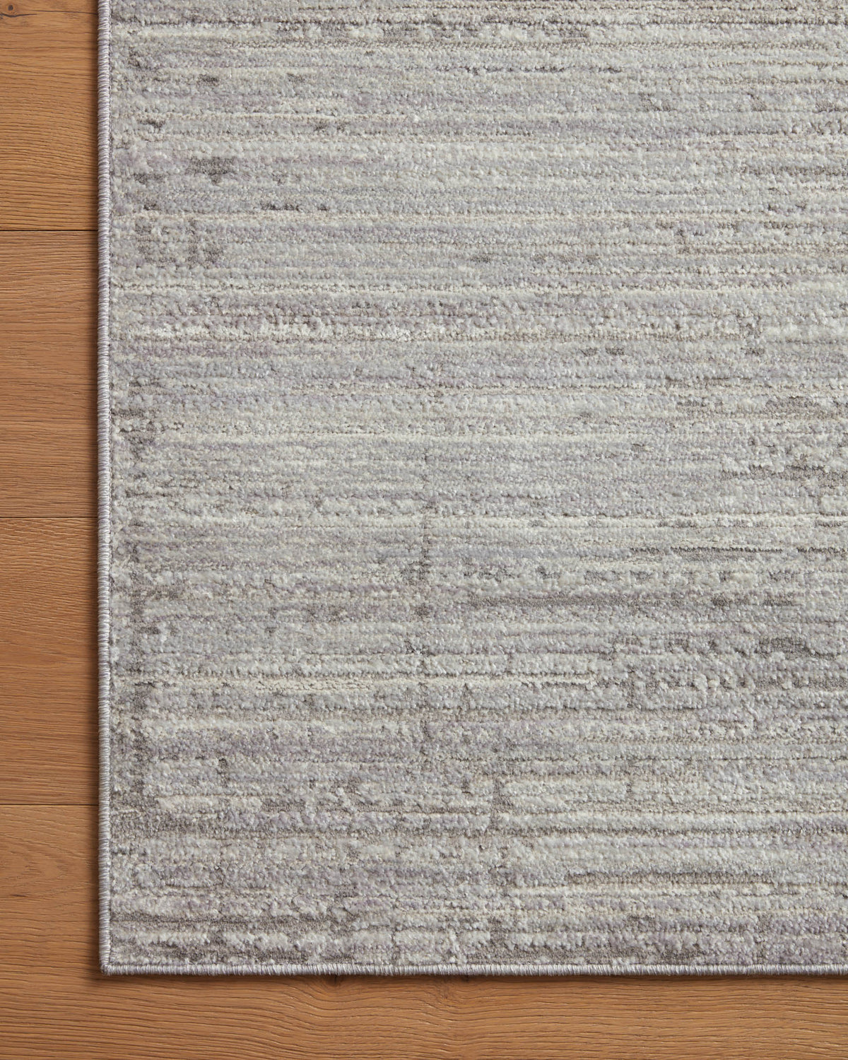 Light grey area rug with textured border and horizontal banded pattern on wood floor.