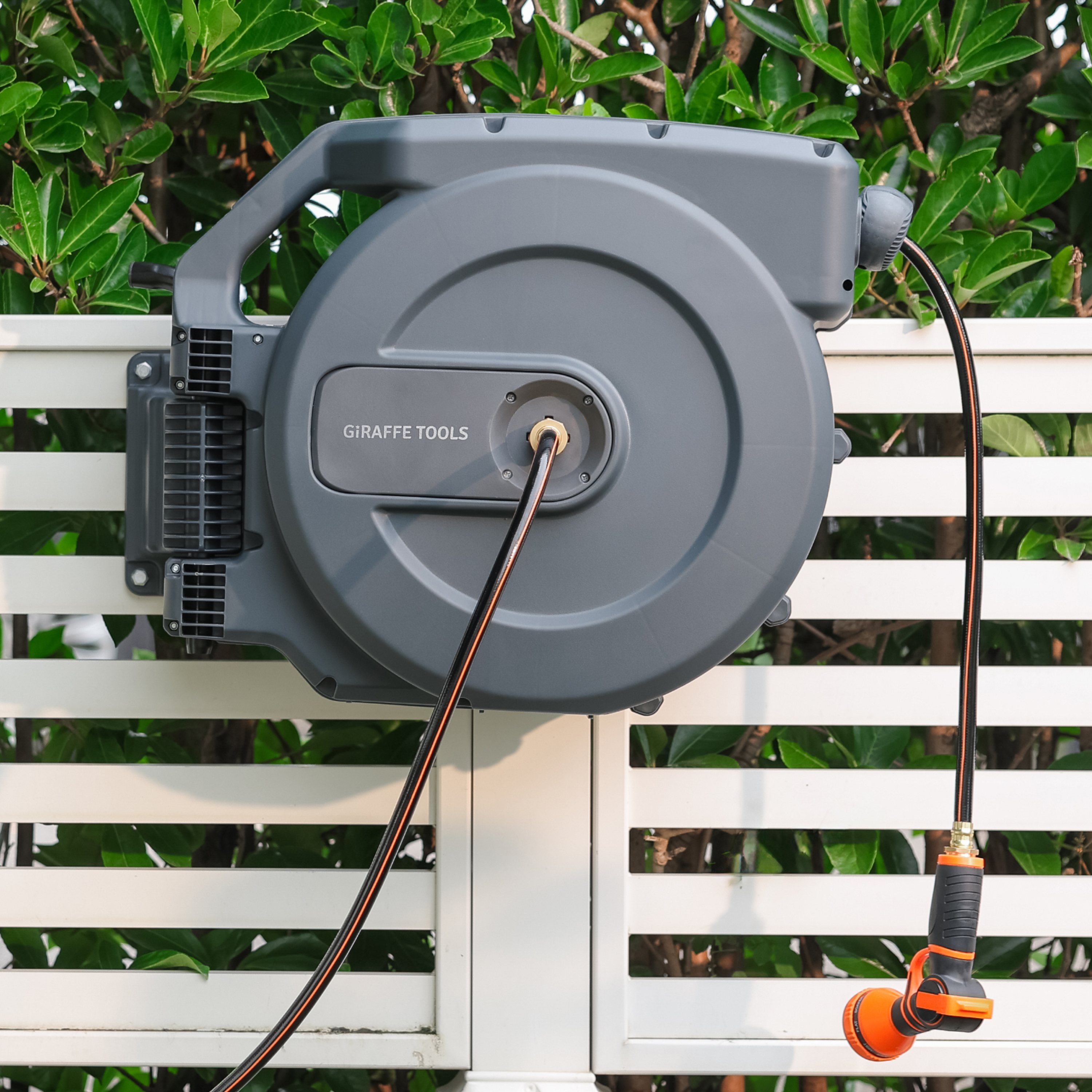 Retractable garden hose reel mounted on a fence with orange hose outlet