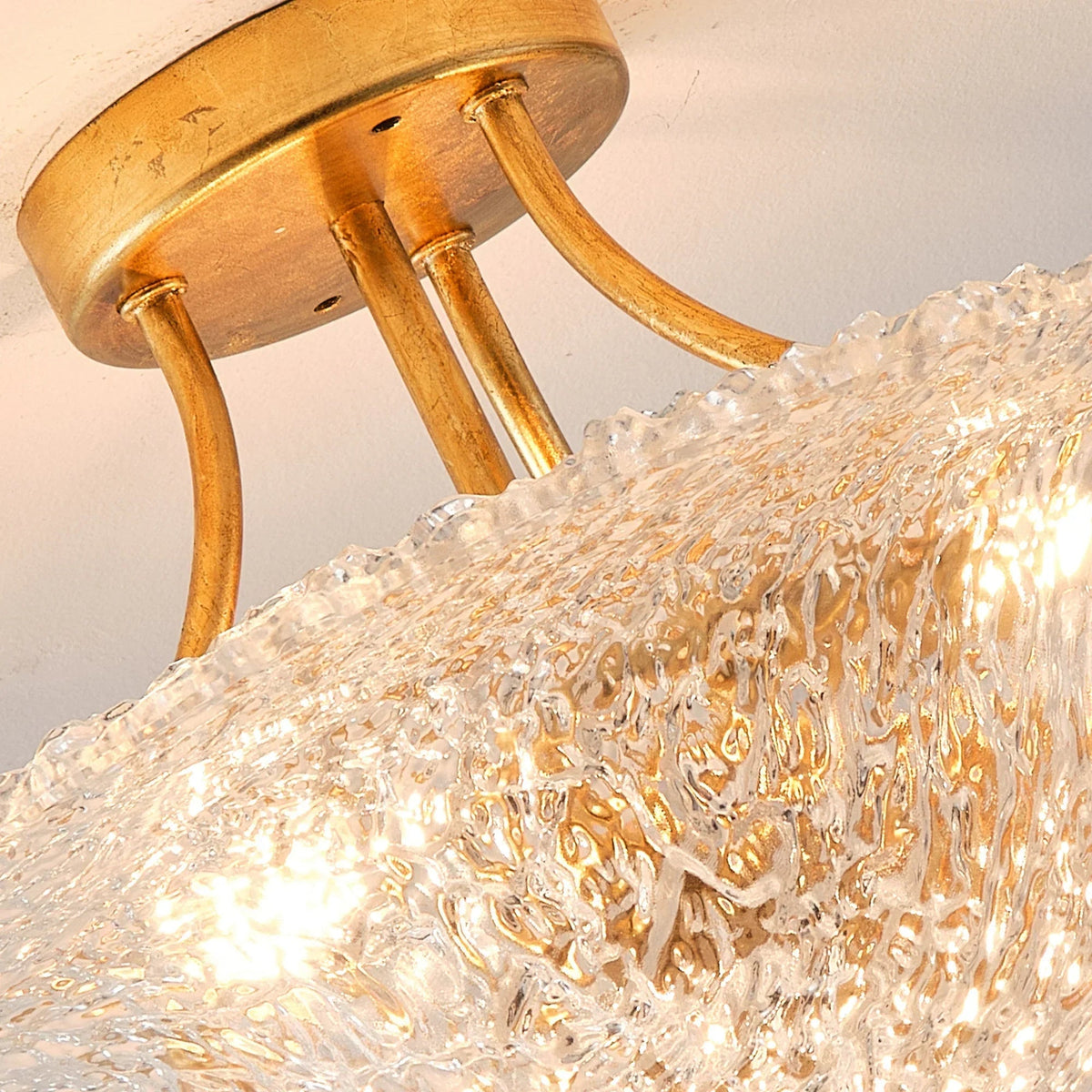 Close-up of golden mounting plate and three curved arms with clear textured shade
