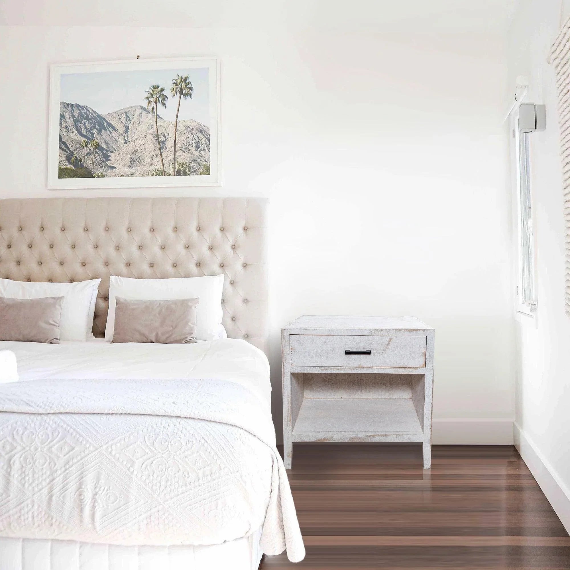 White solid wood nightstand next to bed with single drawer and black pull