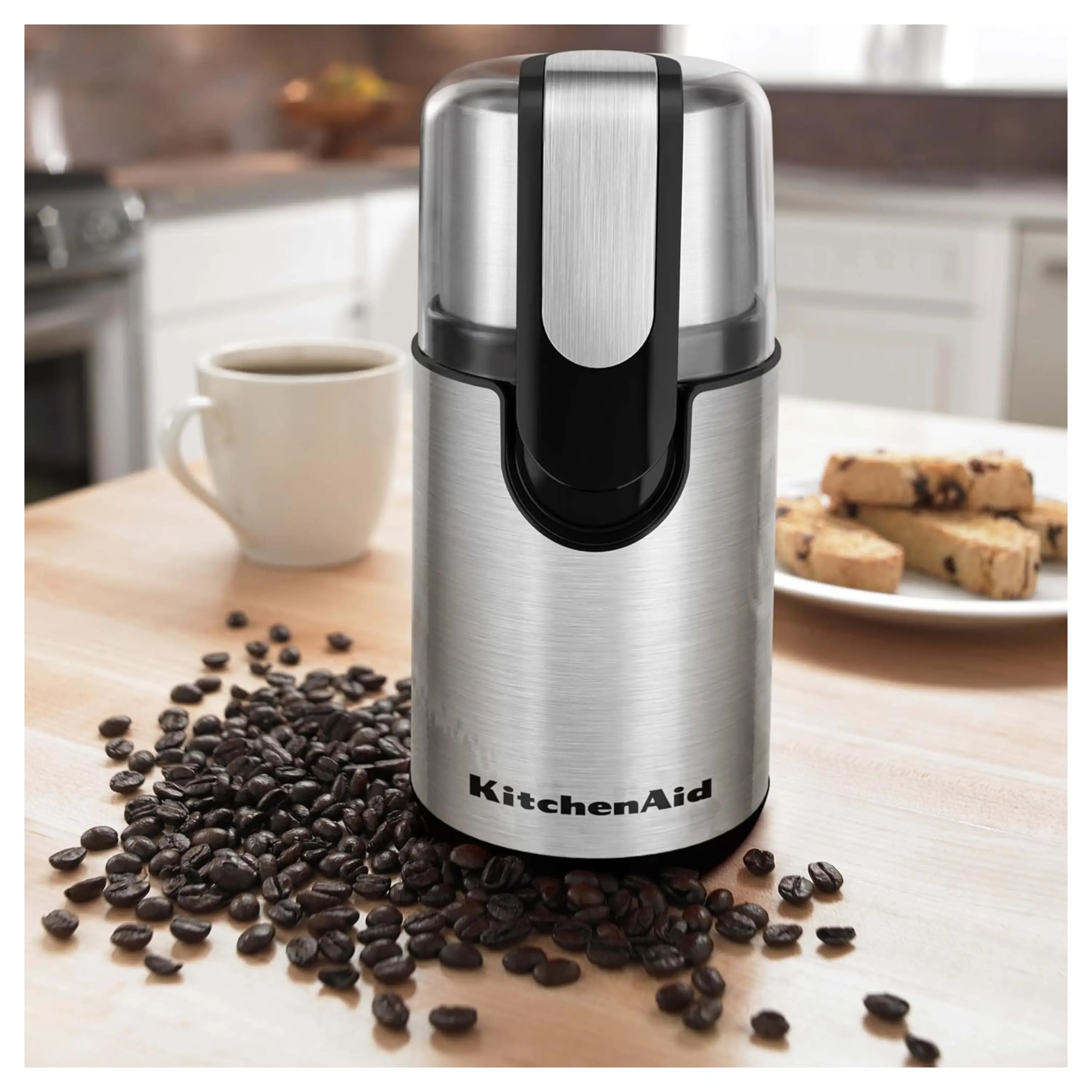 Stainless steel coffee grinder on countertop with scattered coffee beans near base