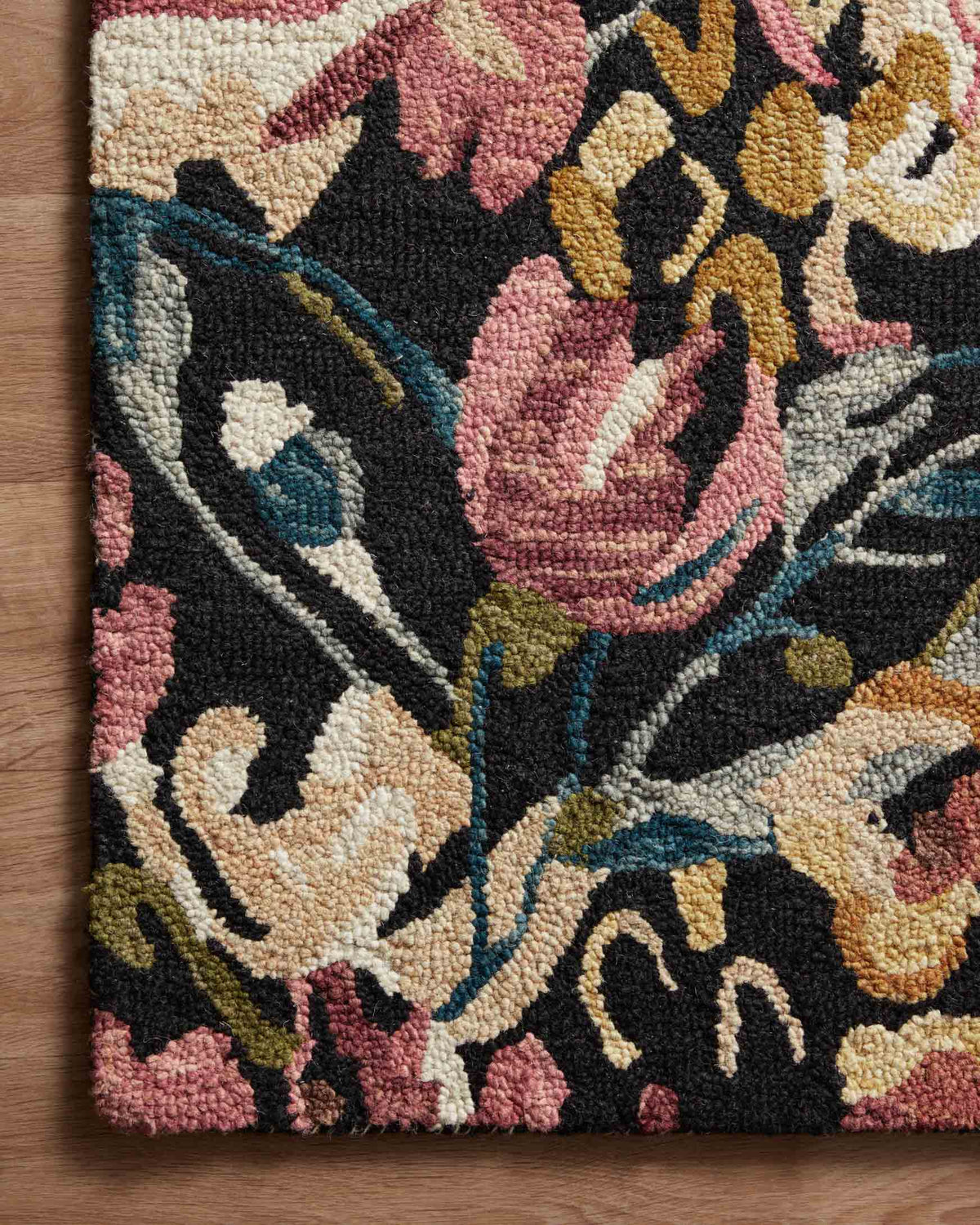 Corner view of black floral rug with pink, cream, and teal accent accents