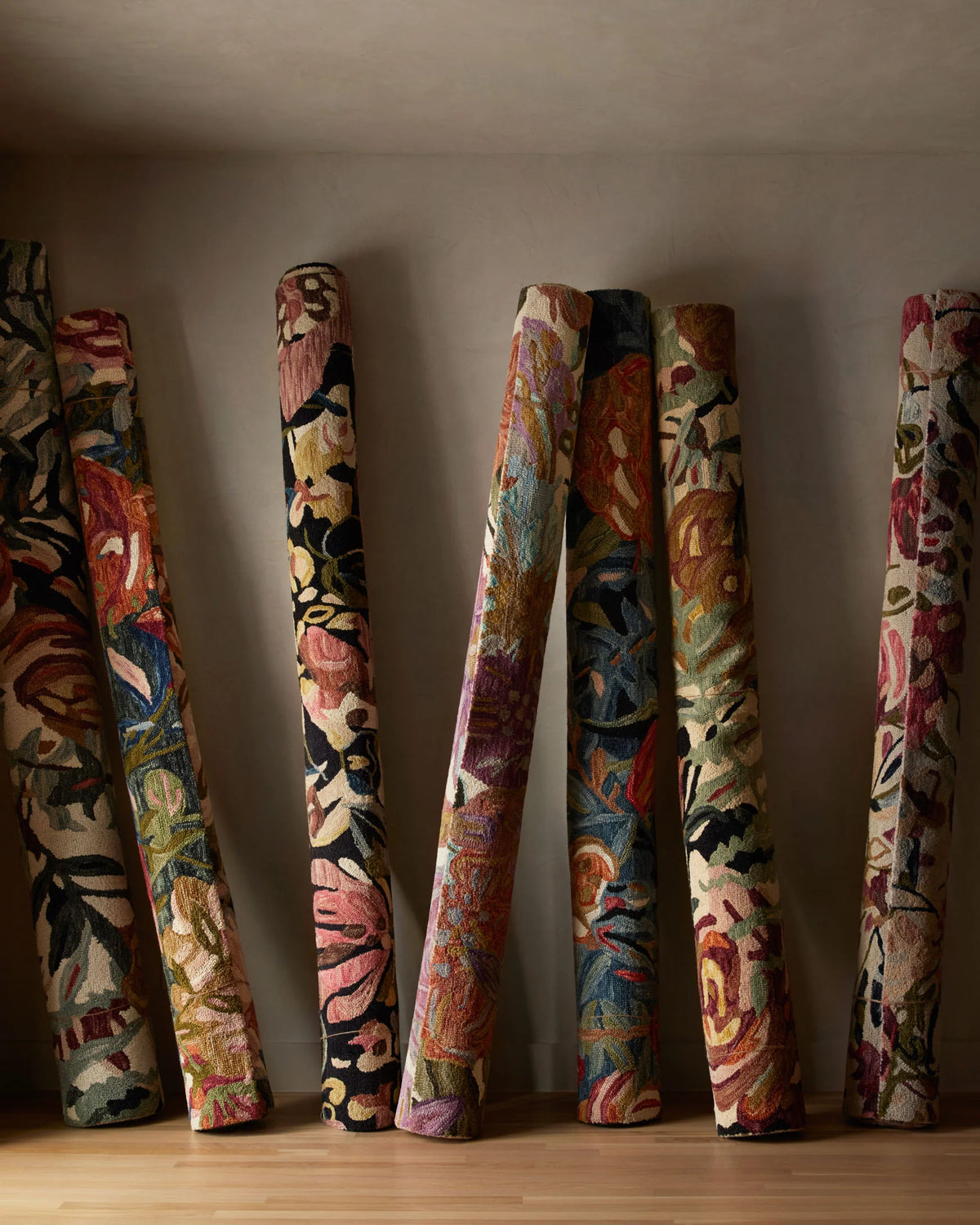 Rolled multicolor floral accent rugs standing upright against a wall