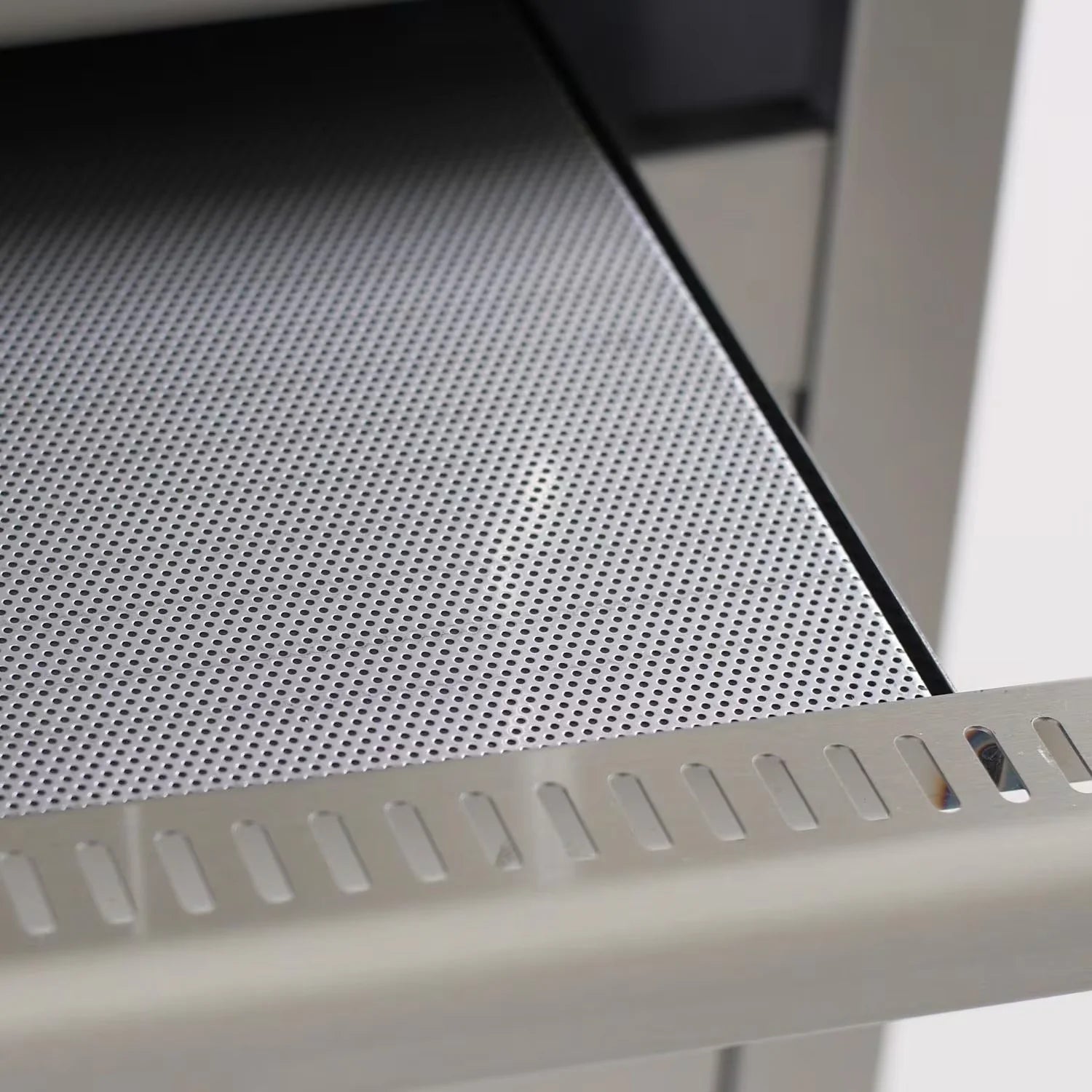 Perforated stainless steel heat shield panel inside open propane grill