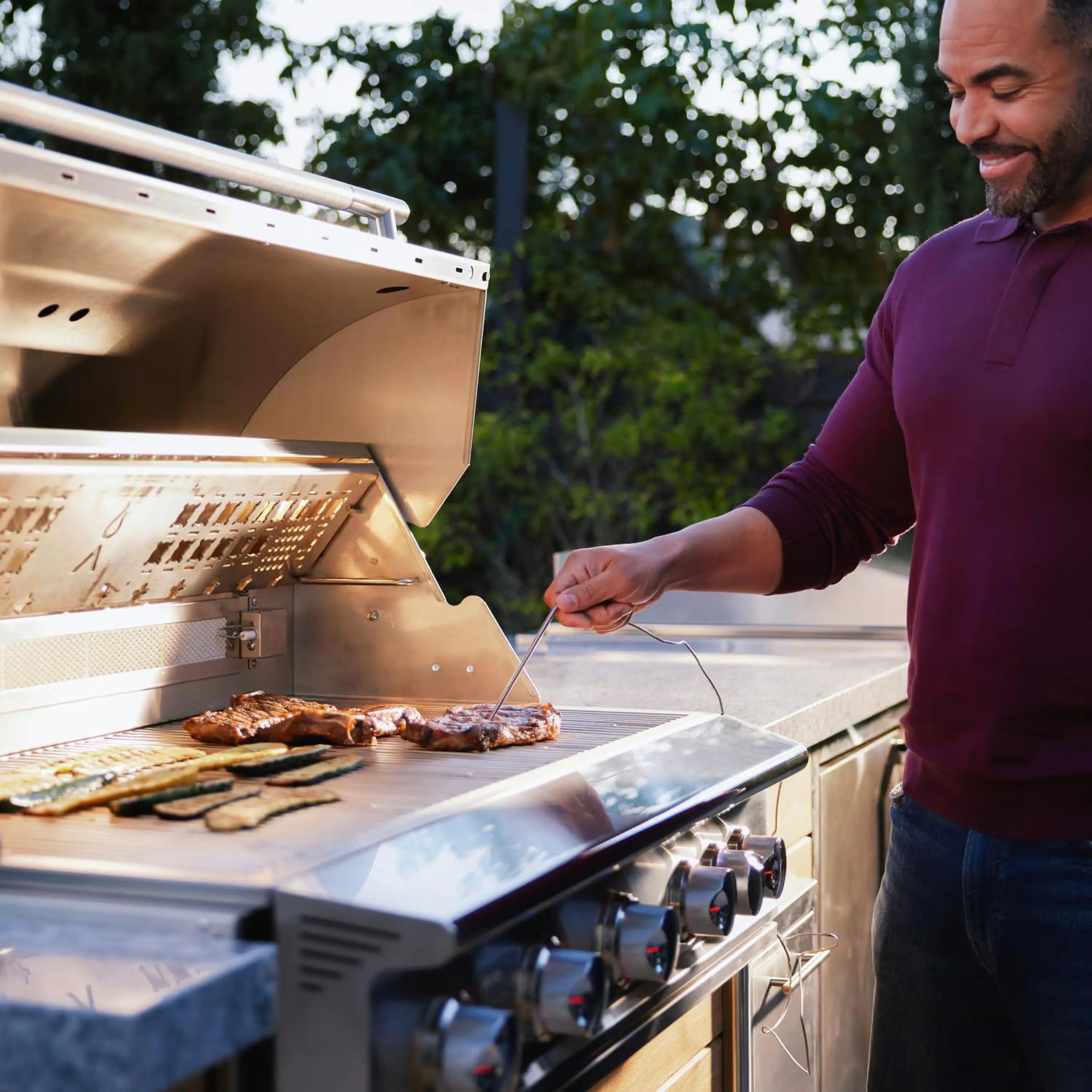 Stainless steel gas grill with open hood showing food grilling on the grates