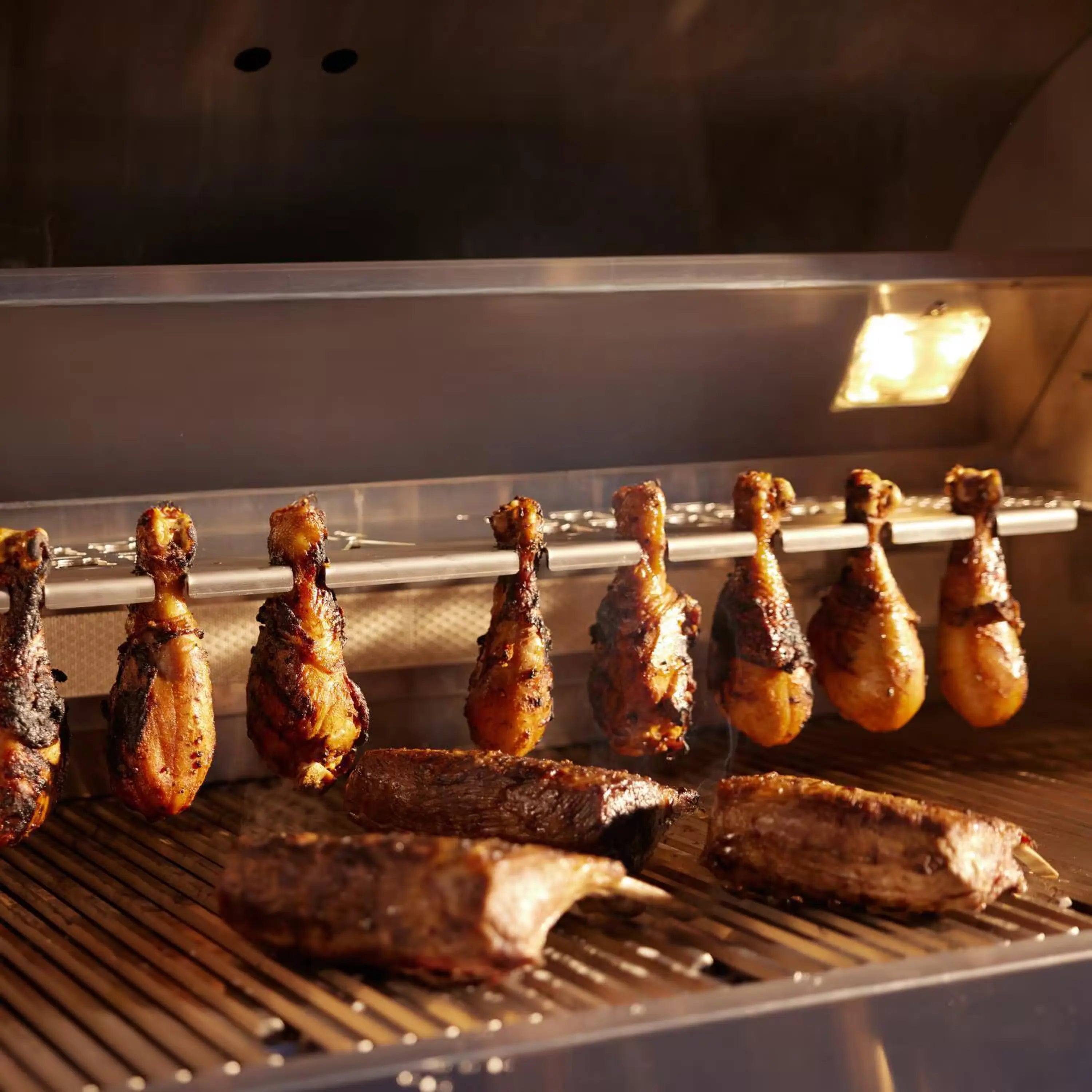 Gas grill interior with glowing burners and browned chicken on the cooking grates
