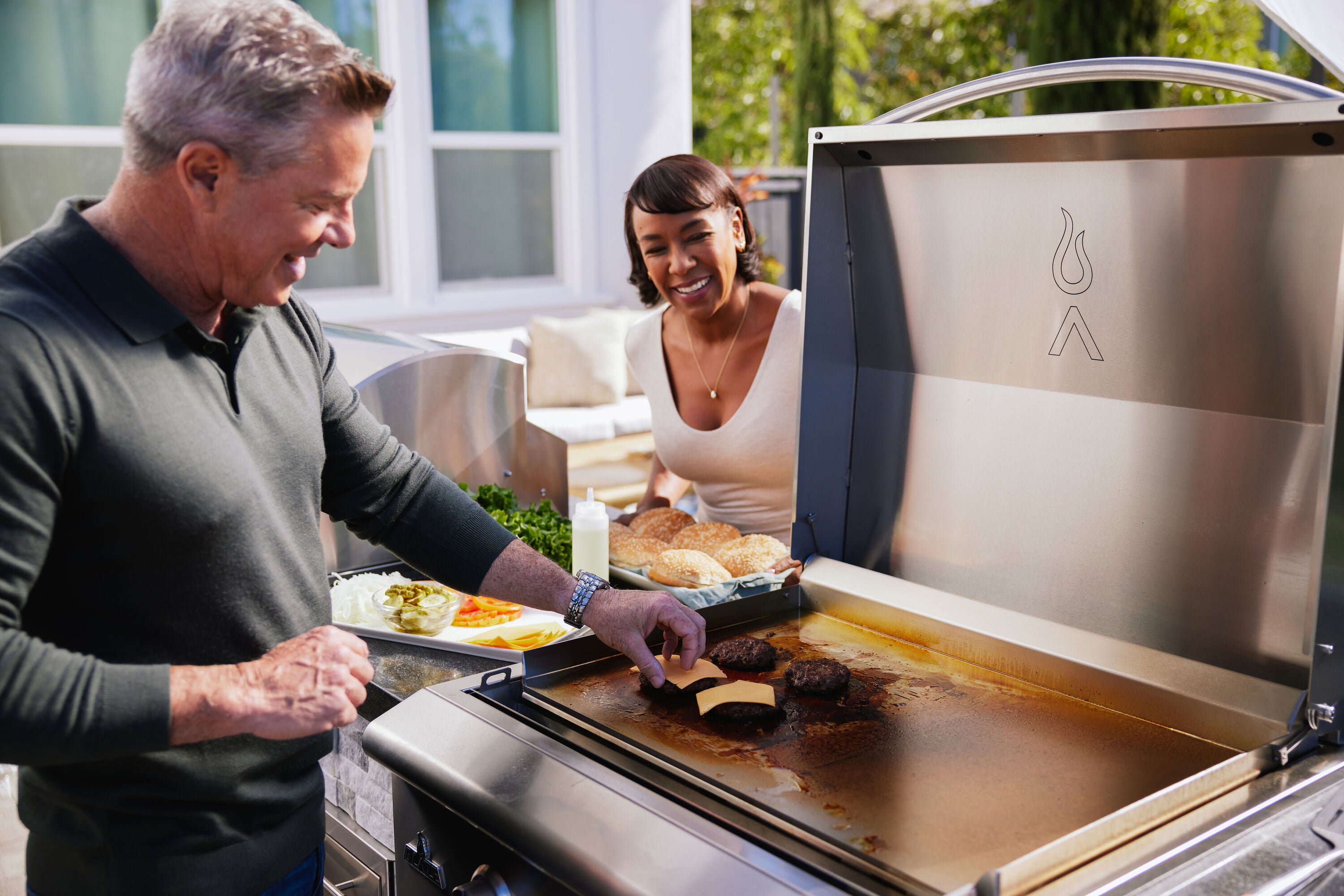 Built-in propane griddle with hood open as food cooks on the flat stainless cooking surface