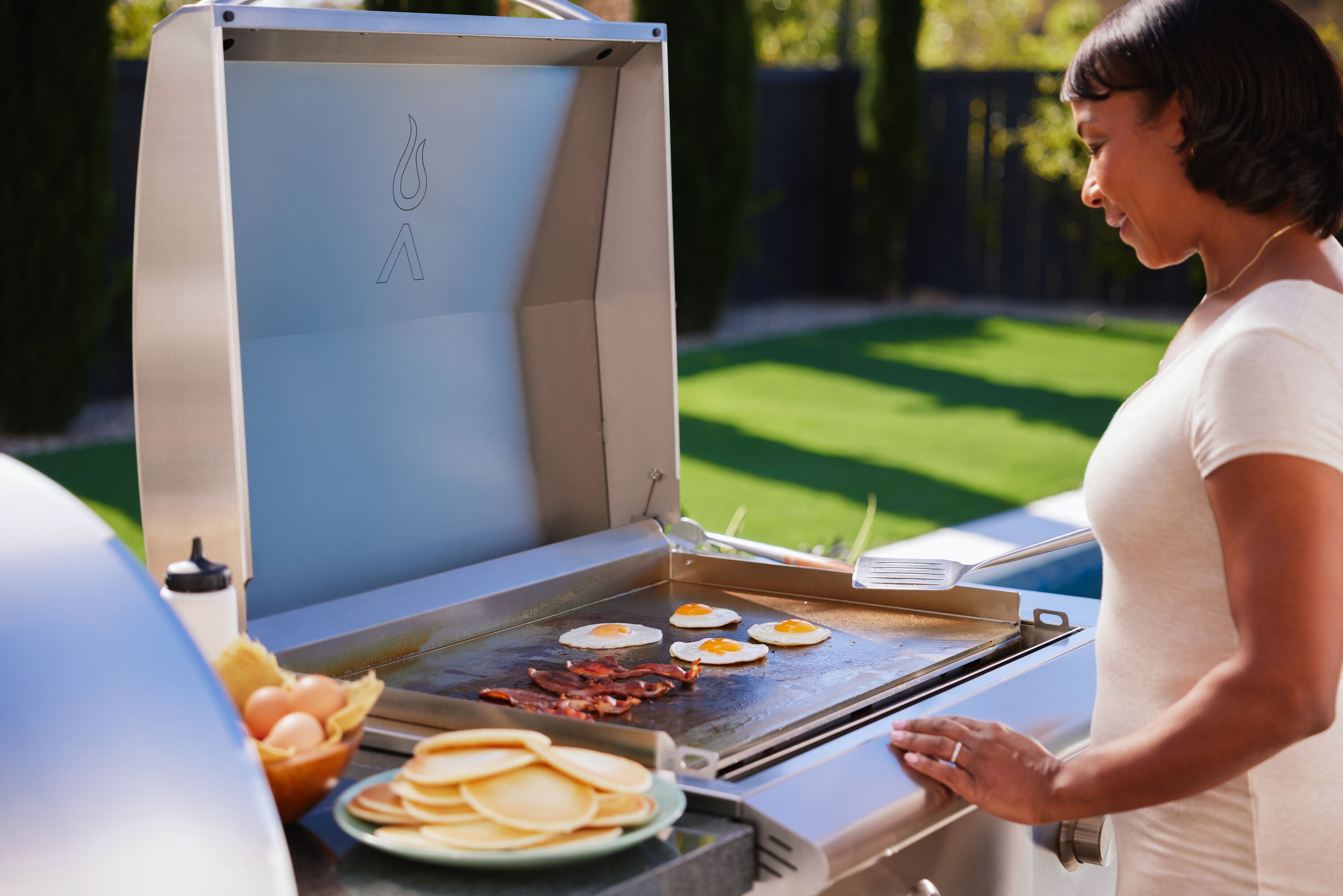 Stainless propane griddle with hood open, pancakes and bacon cooking on the flat griddle top