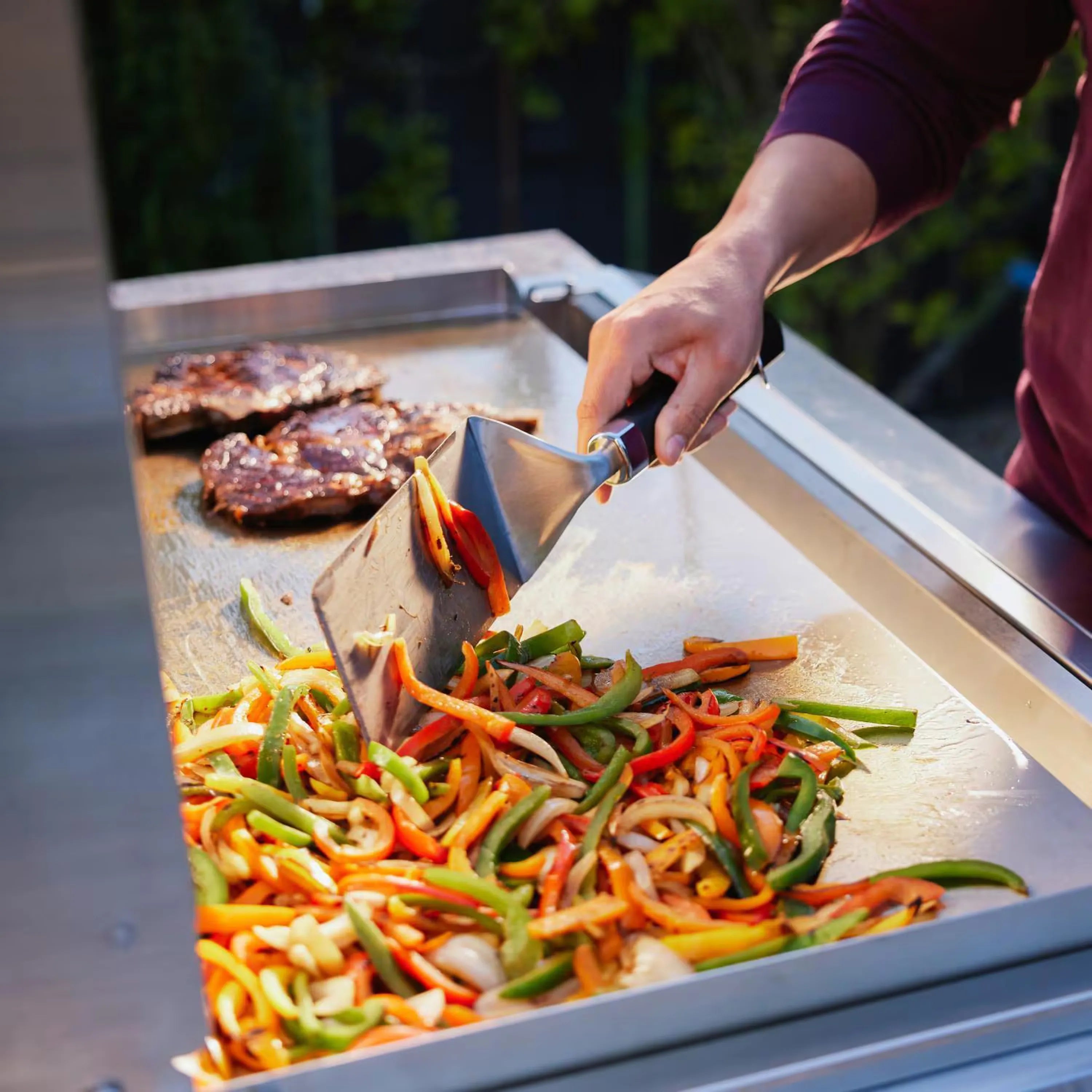 Built-in gas griddle with sliced vegetables and burgers being cooked