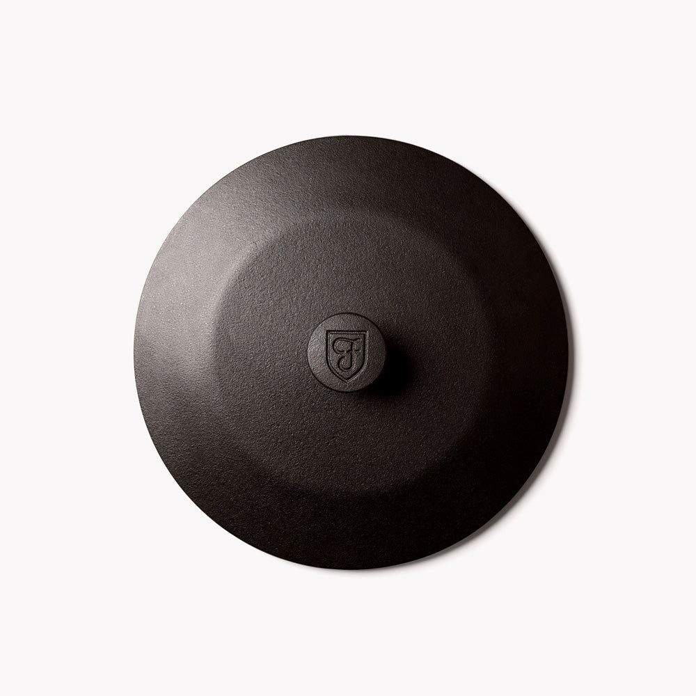 Dark cast-iron lid top with central knob, textured matte finish
