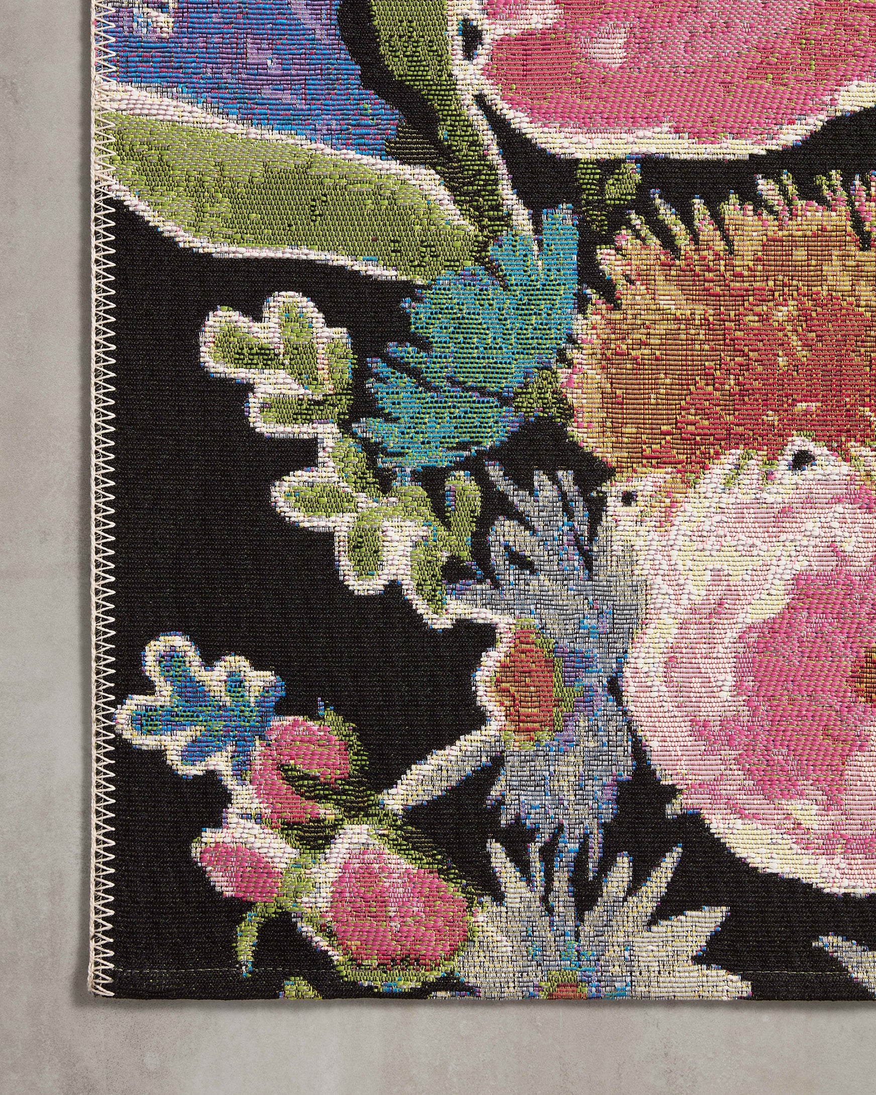 Close-up of woven floral pattern on dark botanical rug with bright pink and green