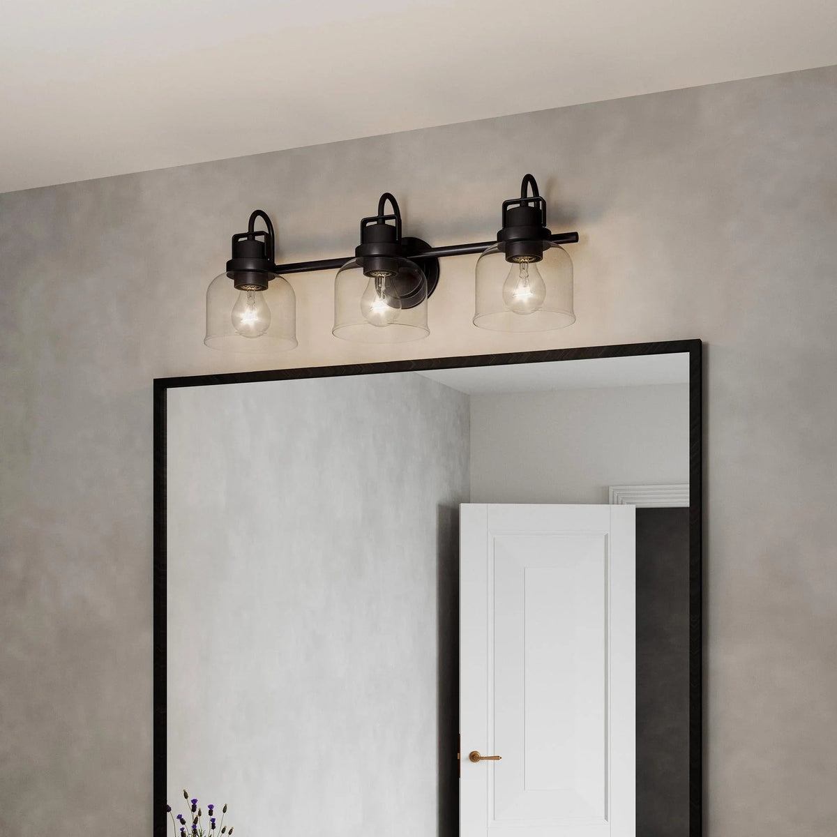 Three-light dark bronze vanity light over a doorway with clear glass shades