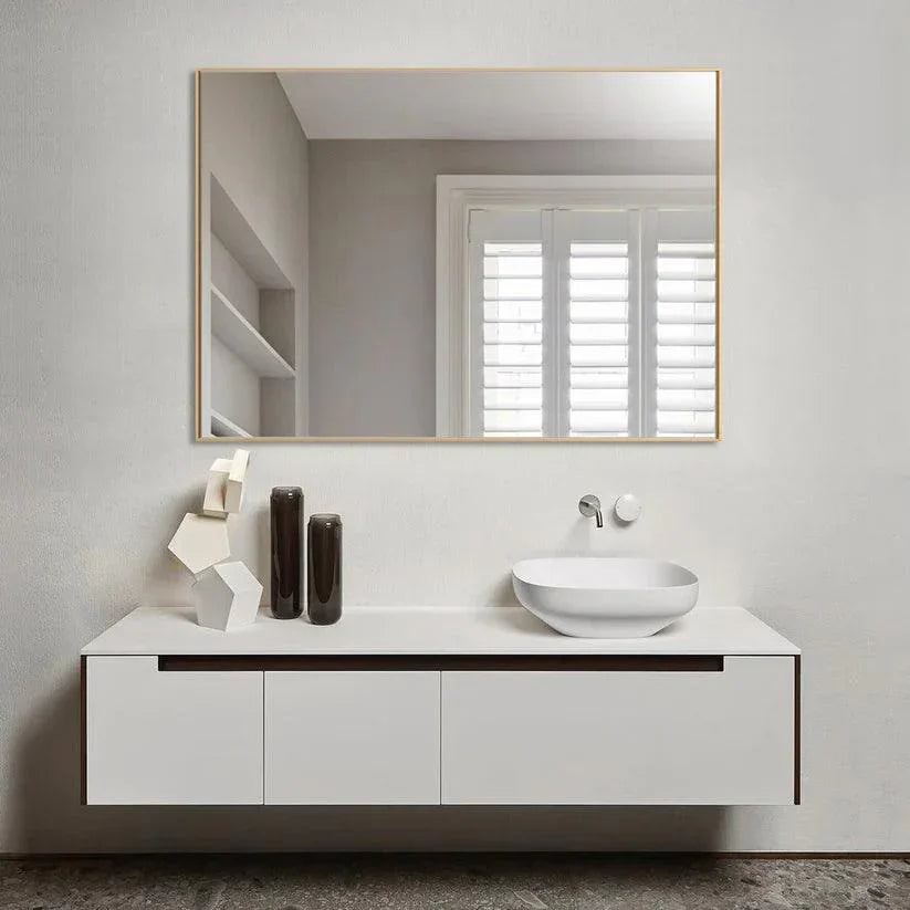 Rectangular wall mirror with golden frame reflecting bathroom sink and shelves