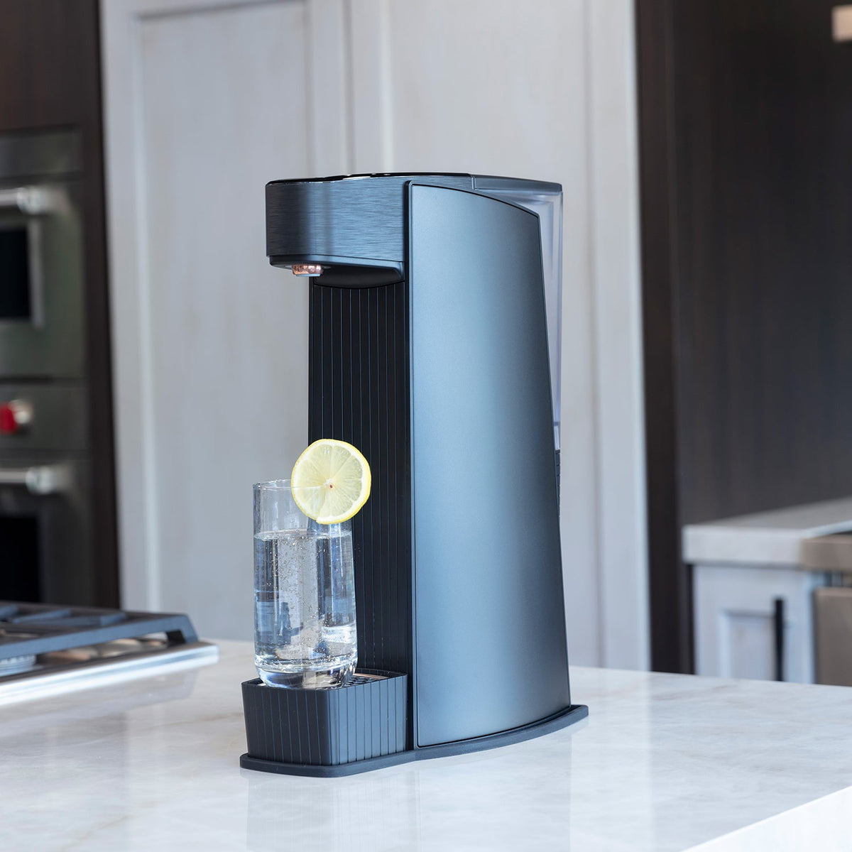 Black sparkling water maker with clear glass and lemon slice on countertop