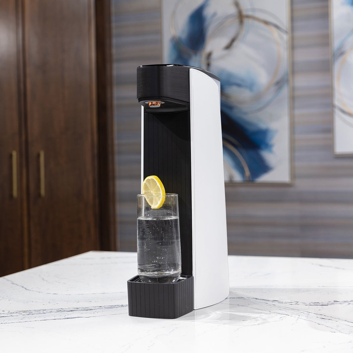 White sparkling water maker with lemon-slice glass on a white marble countertop