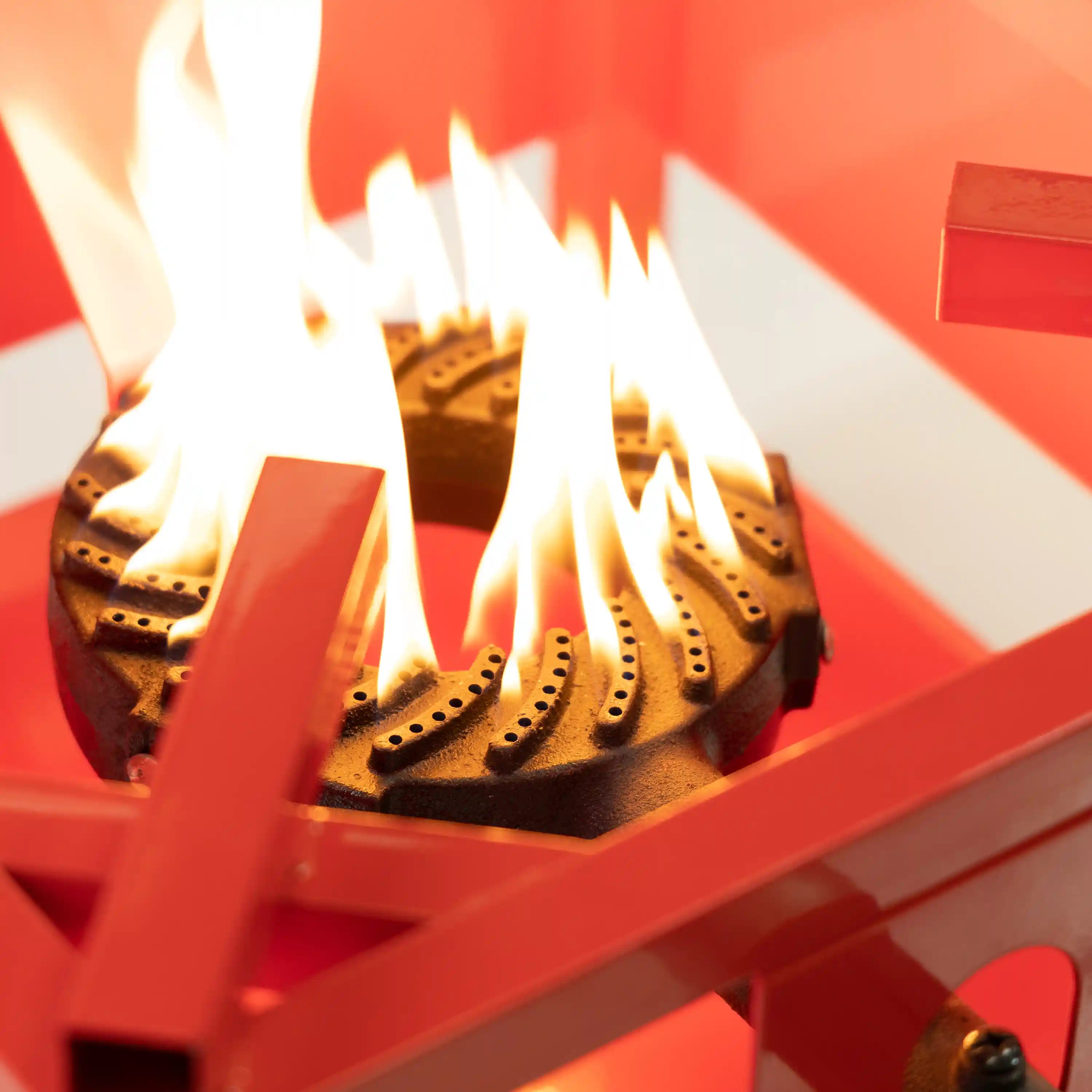 Outdoor propane burner with visible flame over metal burner ports inside frame