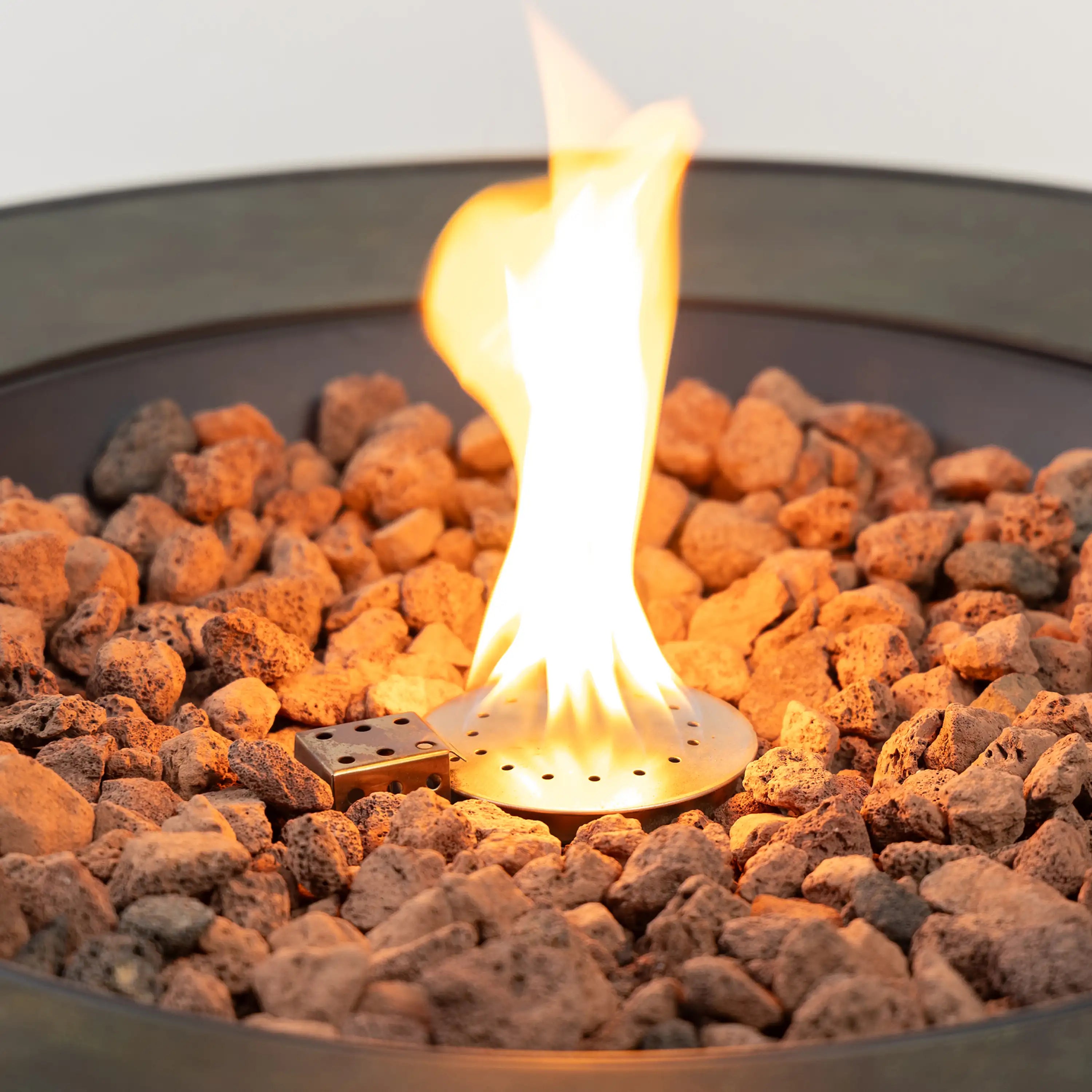 Flame burning over lava rocks inside a black circular gas fire pit