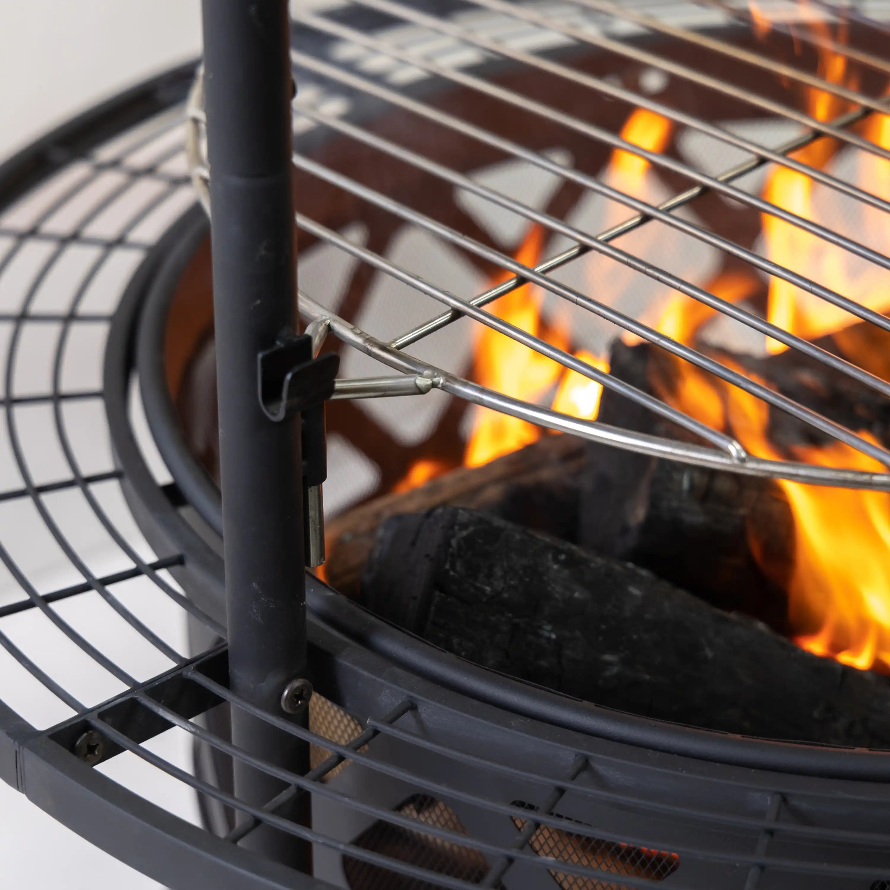 Close-up of black fire pit bowl with wire grate ring and visible orange flames