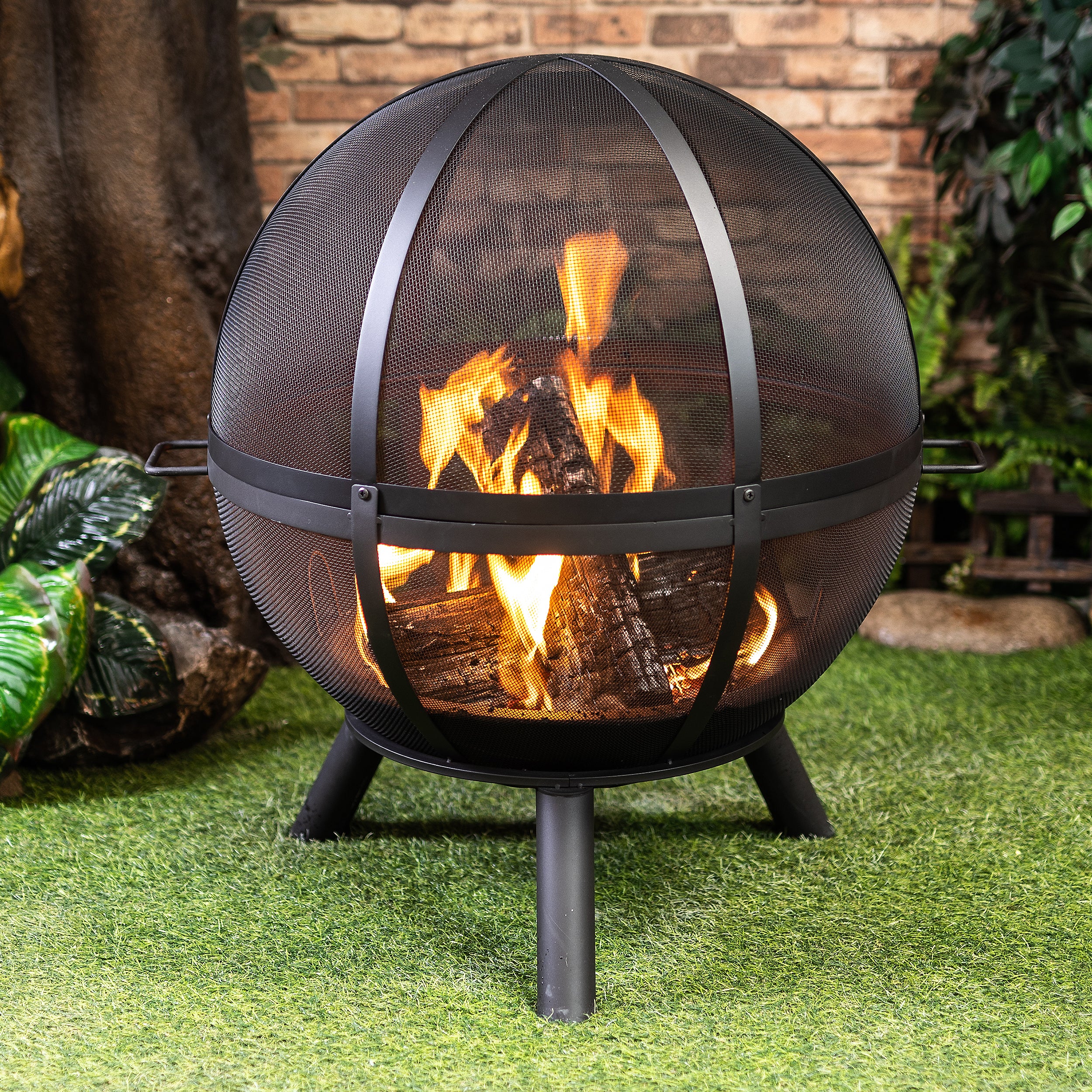 Outdoor sphere woodburning fire pit with black mesh dome and burning flames, on three legs