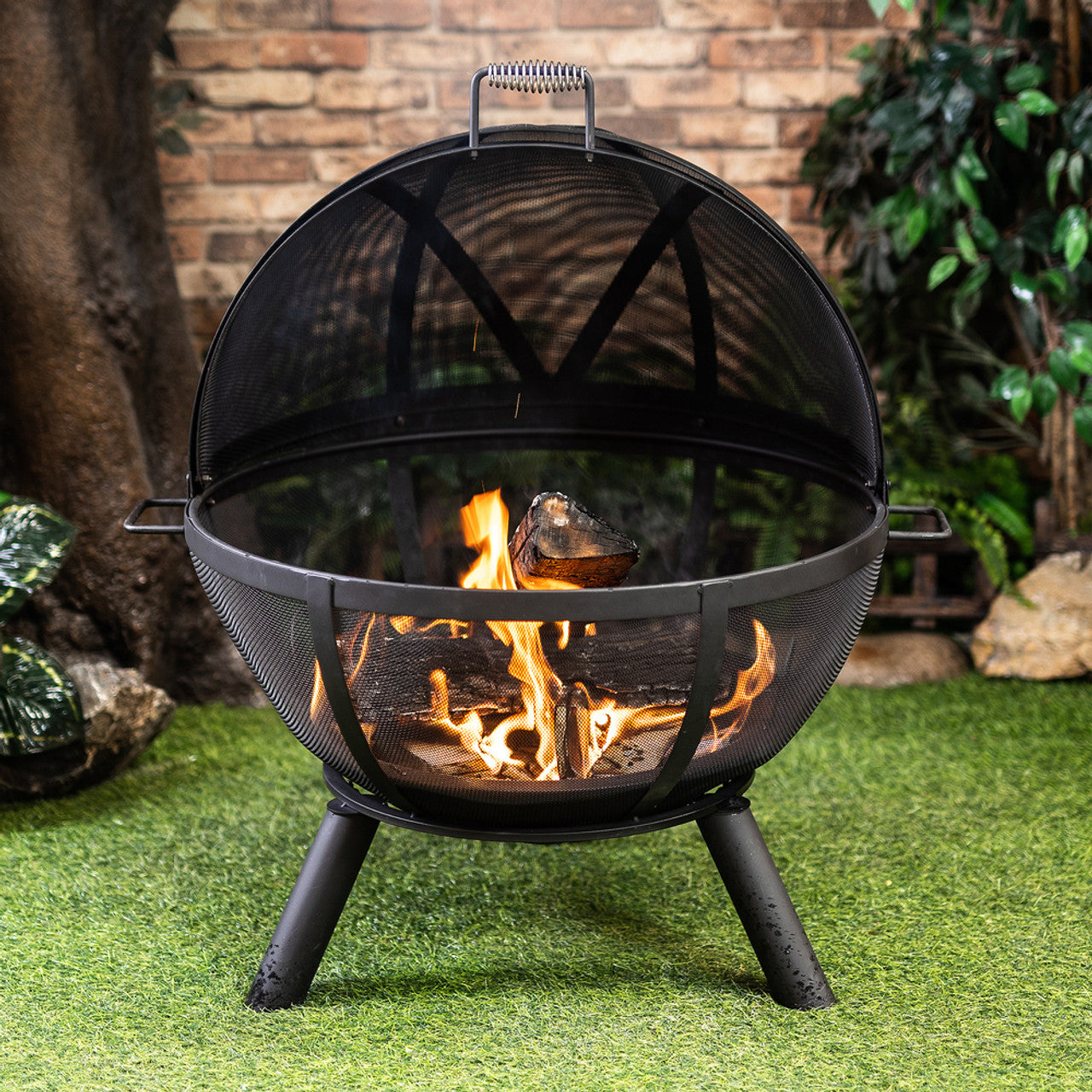 Black mesh dome sphere fire pit with burning wood and front guard, tripod legs