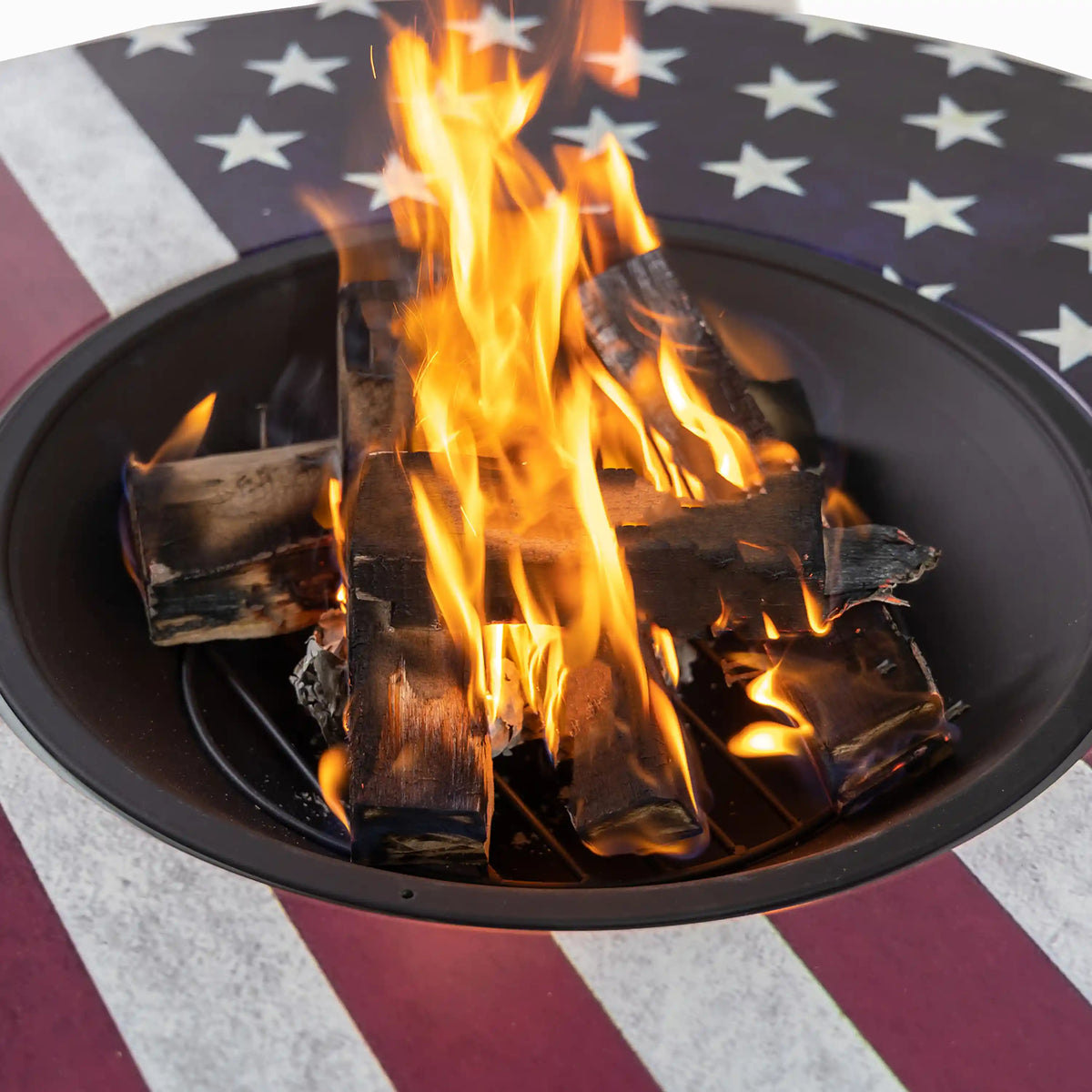 Burning logs rising up from the center opening of a black round fire pit