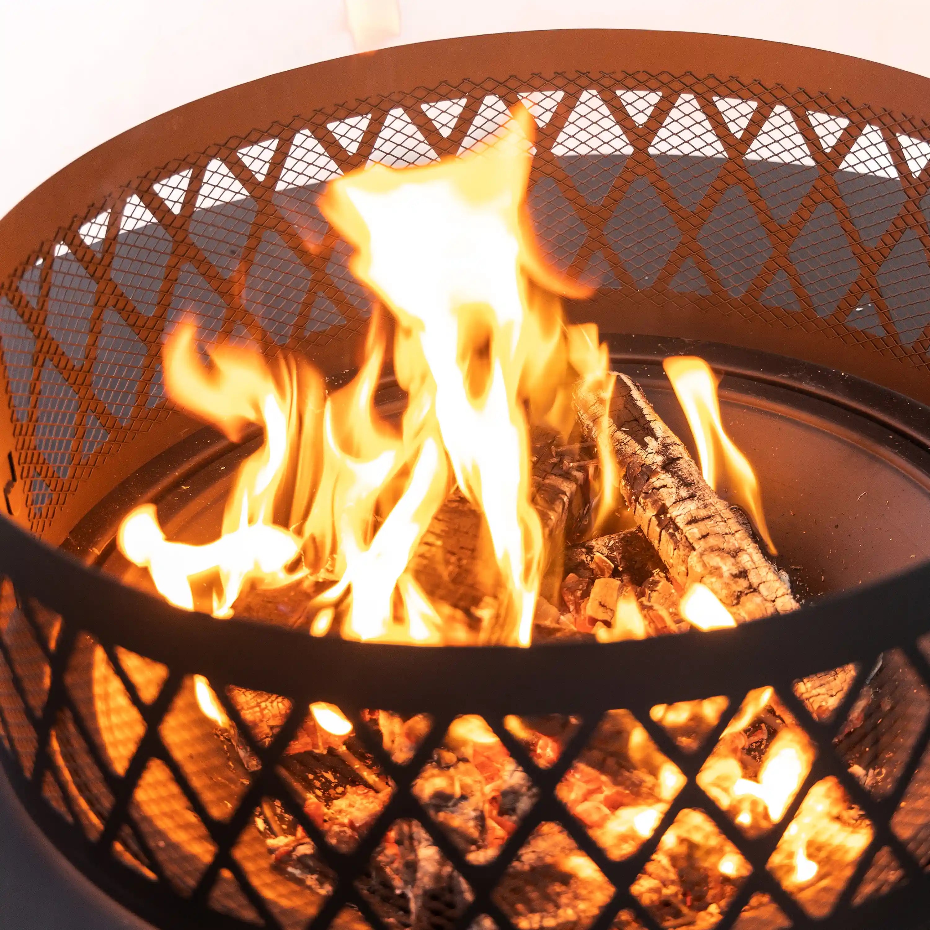 Close-up of flames inside black steel fire bowl with diamond lattice guard.