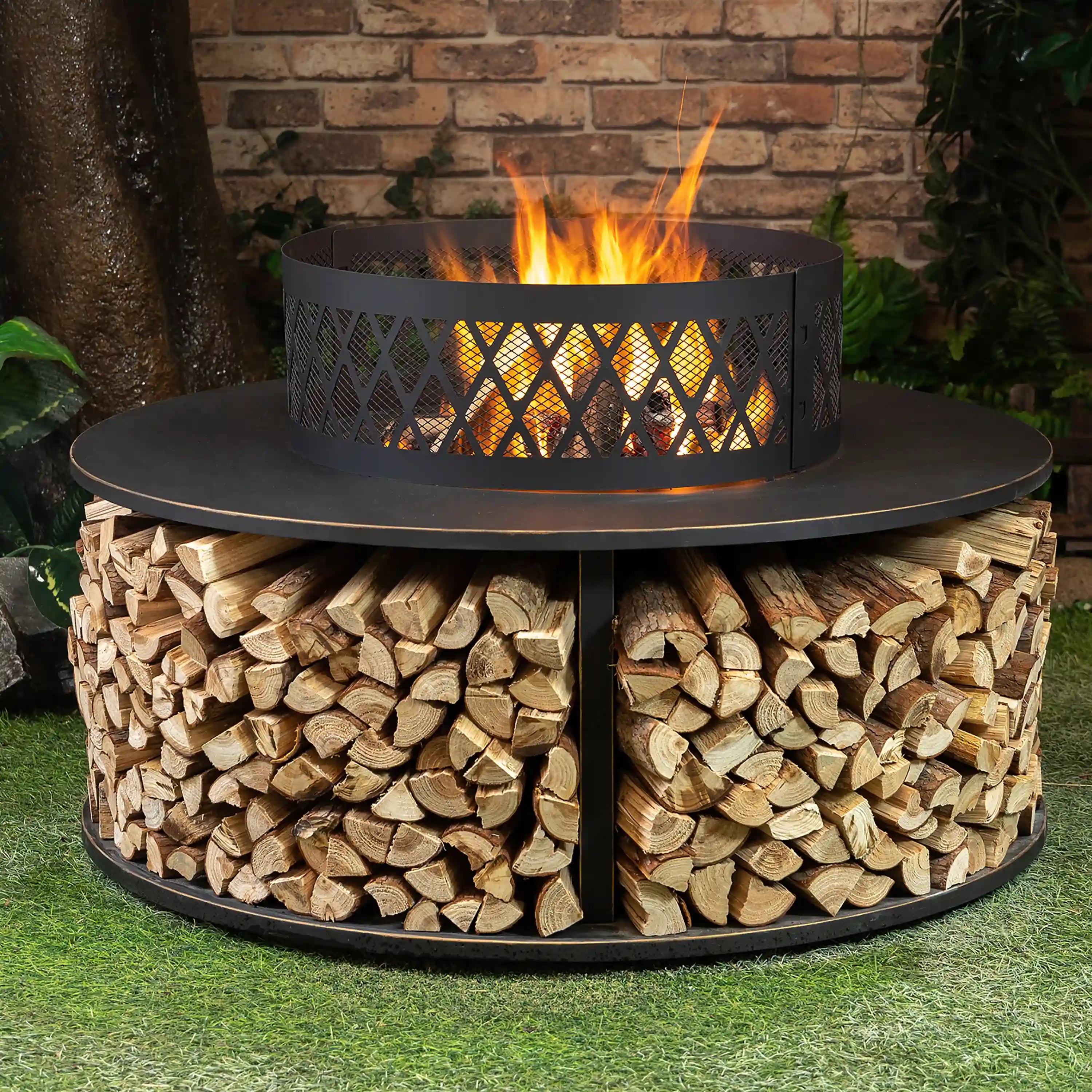 Outdoor fire pit showing flames in mesh bowl atop stacked firewood log storage.