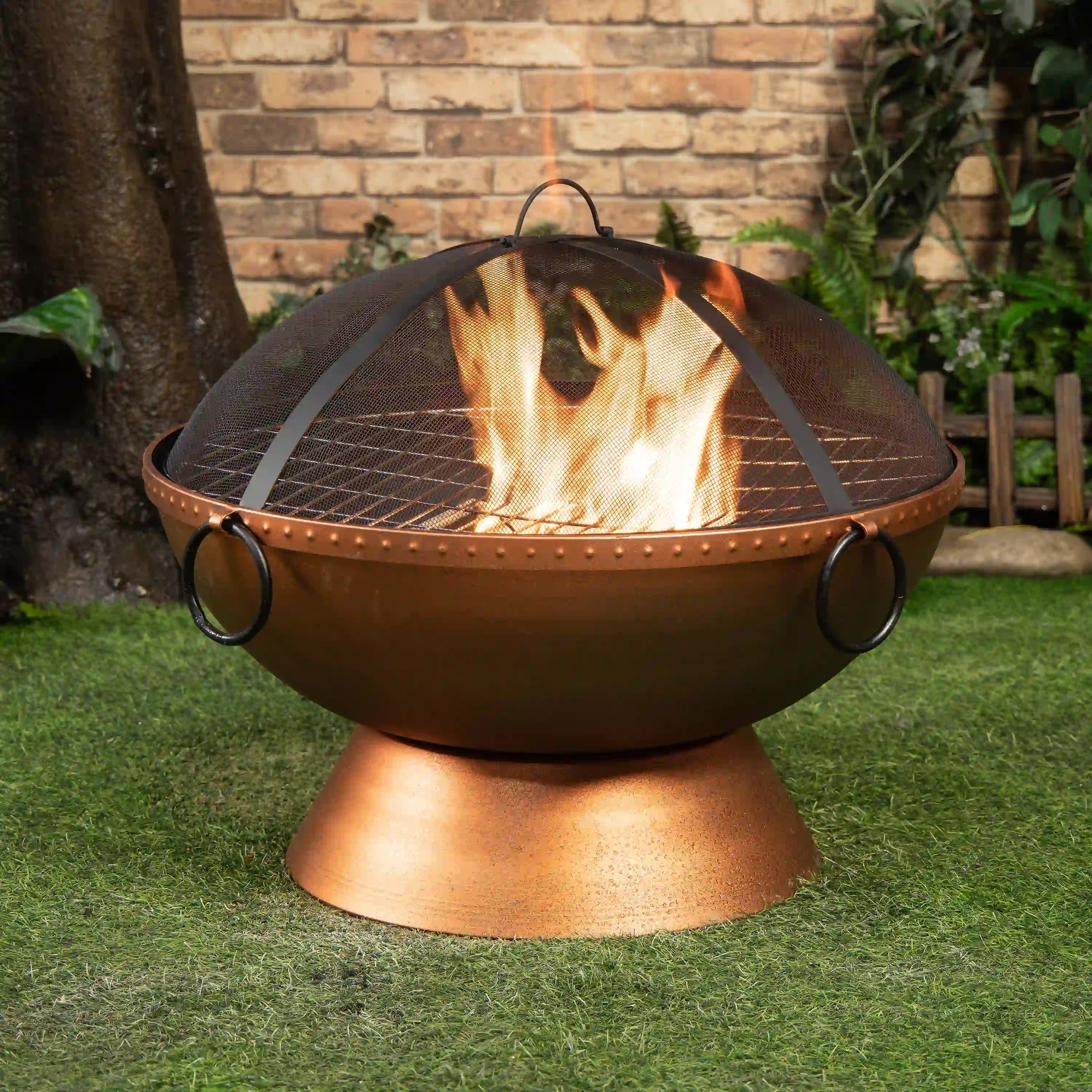 Outdoor round firepit with mesh spark screen, side handles, and visible flames