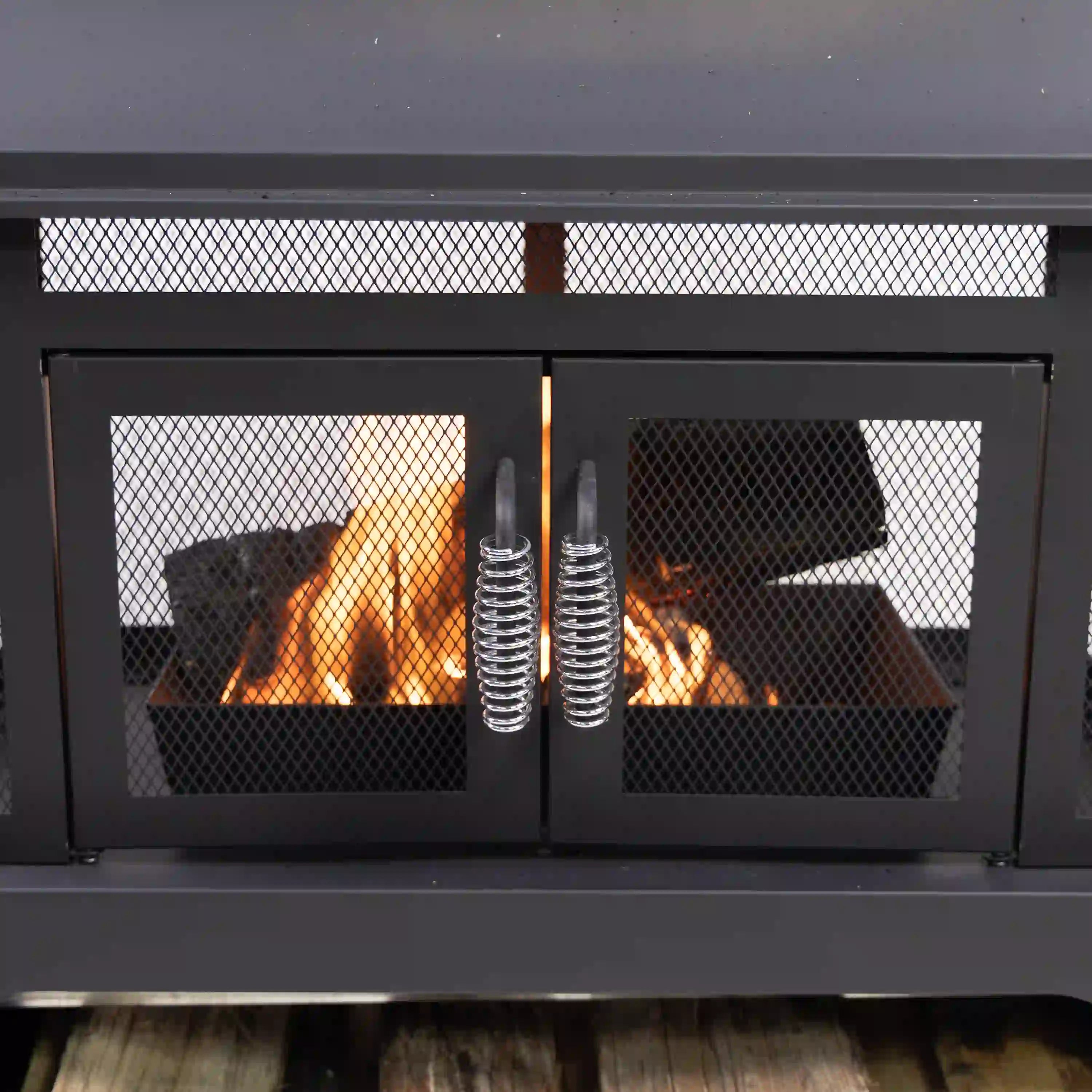 Outdoor rectangular steel wood-burning fireplace with mesh doors and visible flames