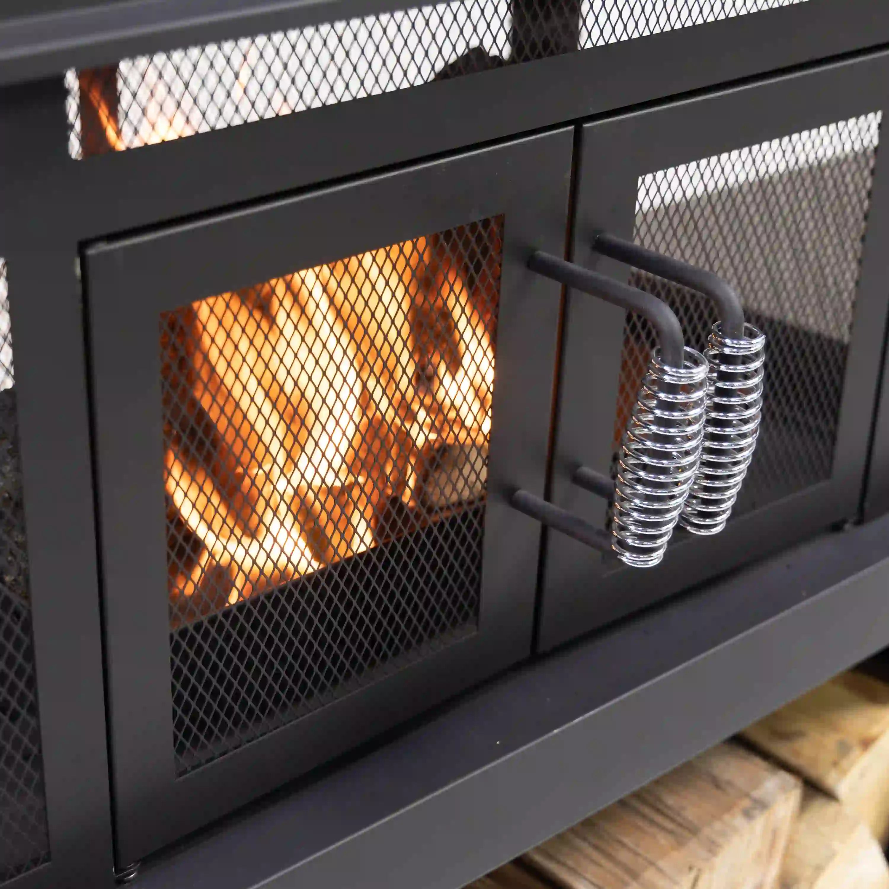 Black outdoor fireplace with mesh front and visible flames behind safety screen