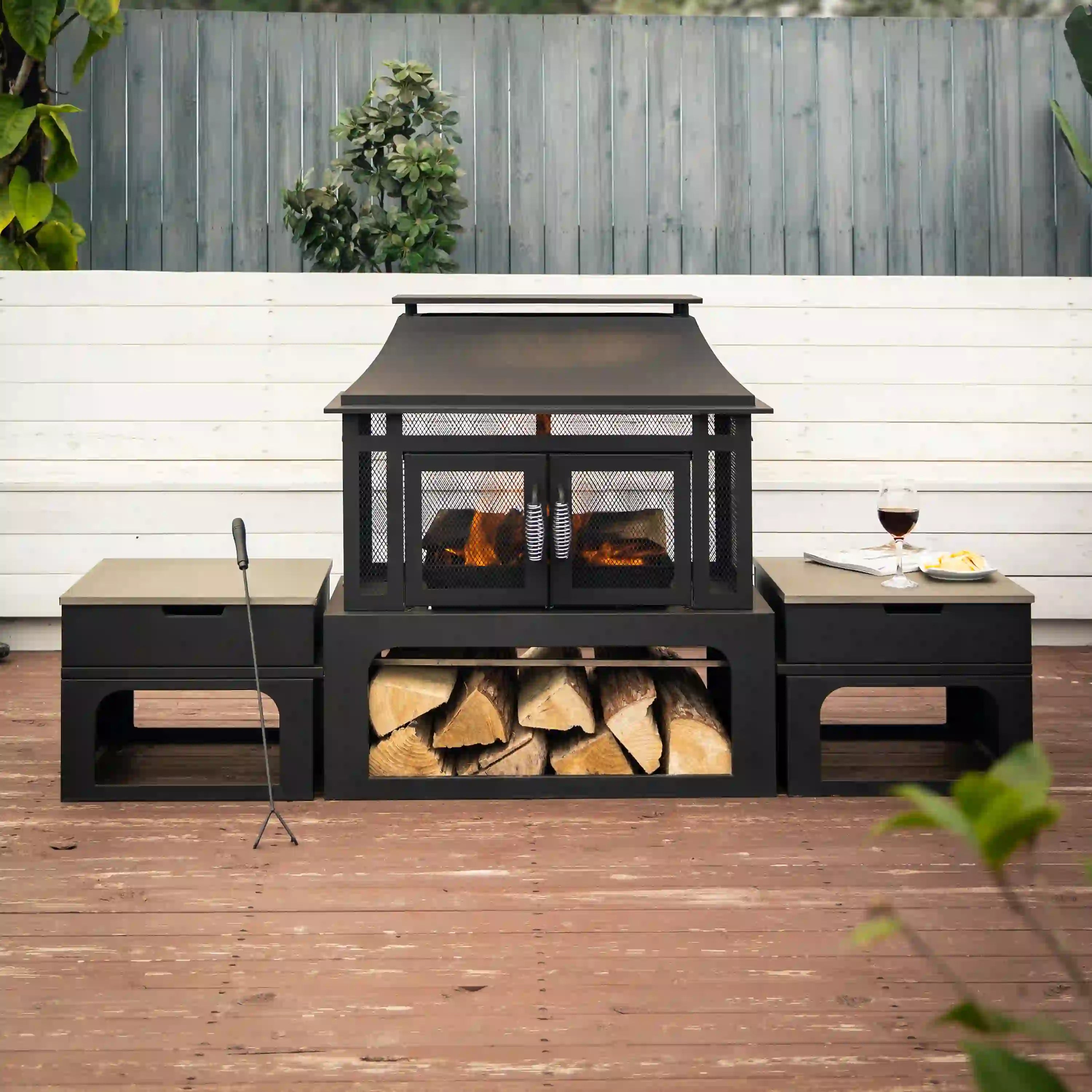 Outdoor patio wood-burning fireplace with side tables, firebox flames, and log bin