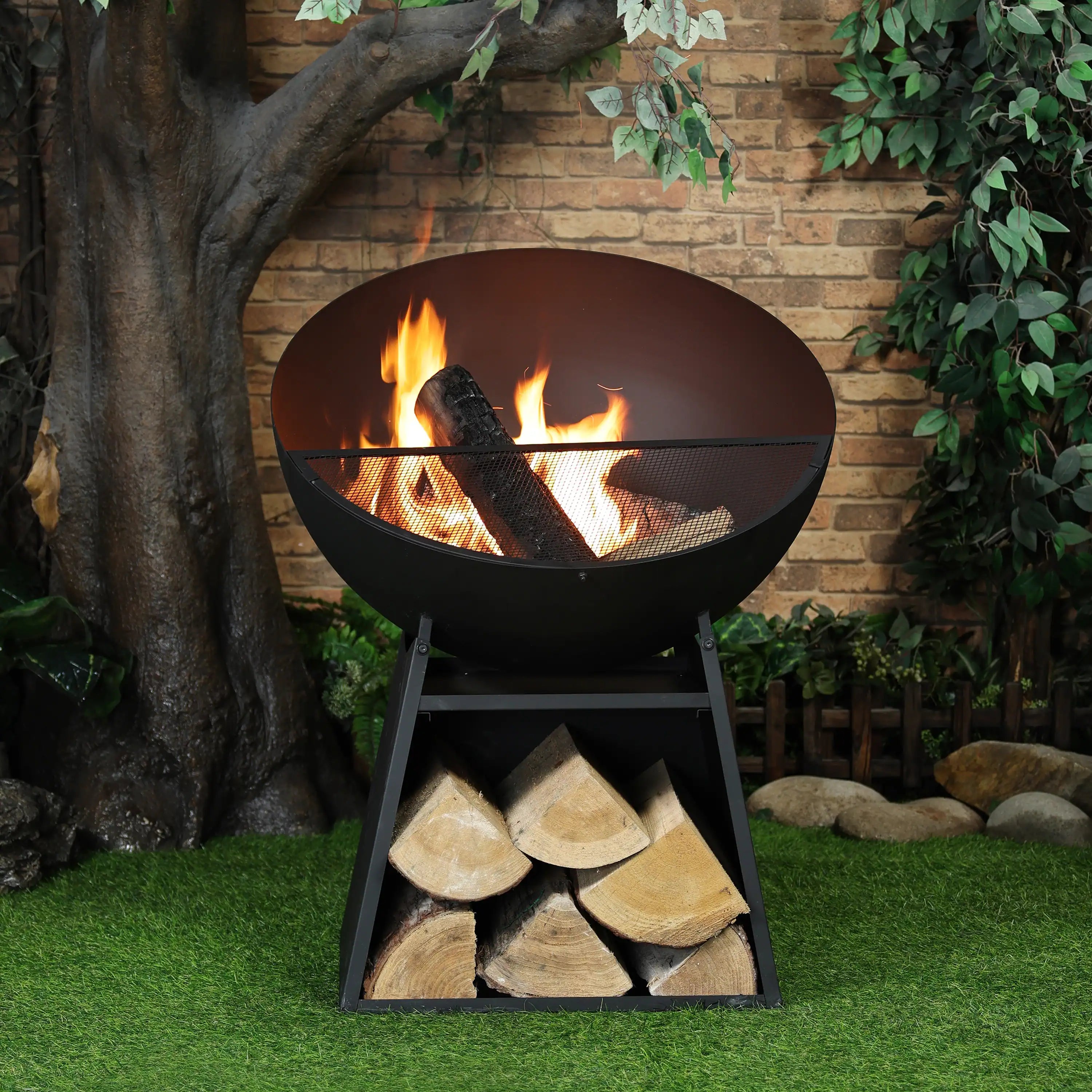 Black round fire pit with mesh spark screen and burning logs on a stand.