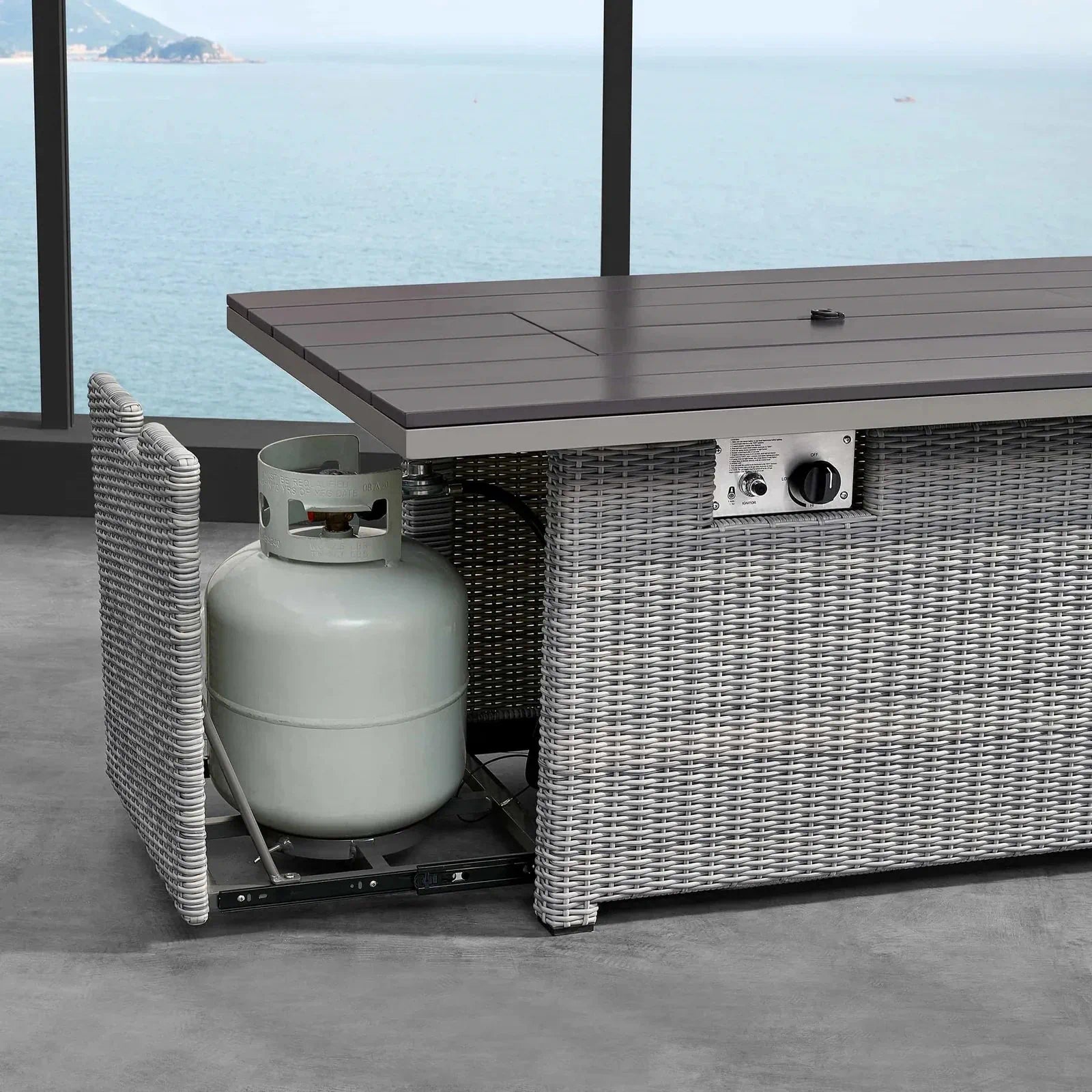 Outdoor fire pit table with gray wicker base and lid panel, showing gas control area