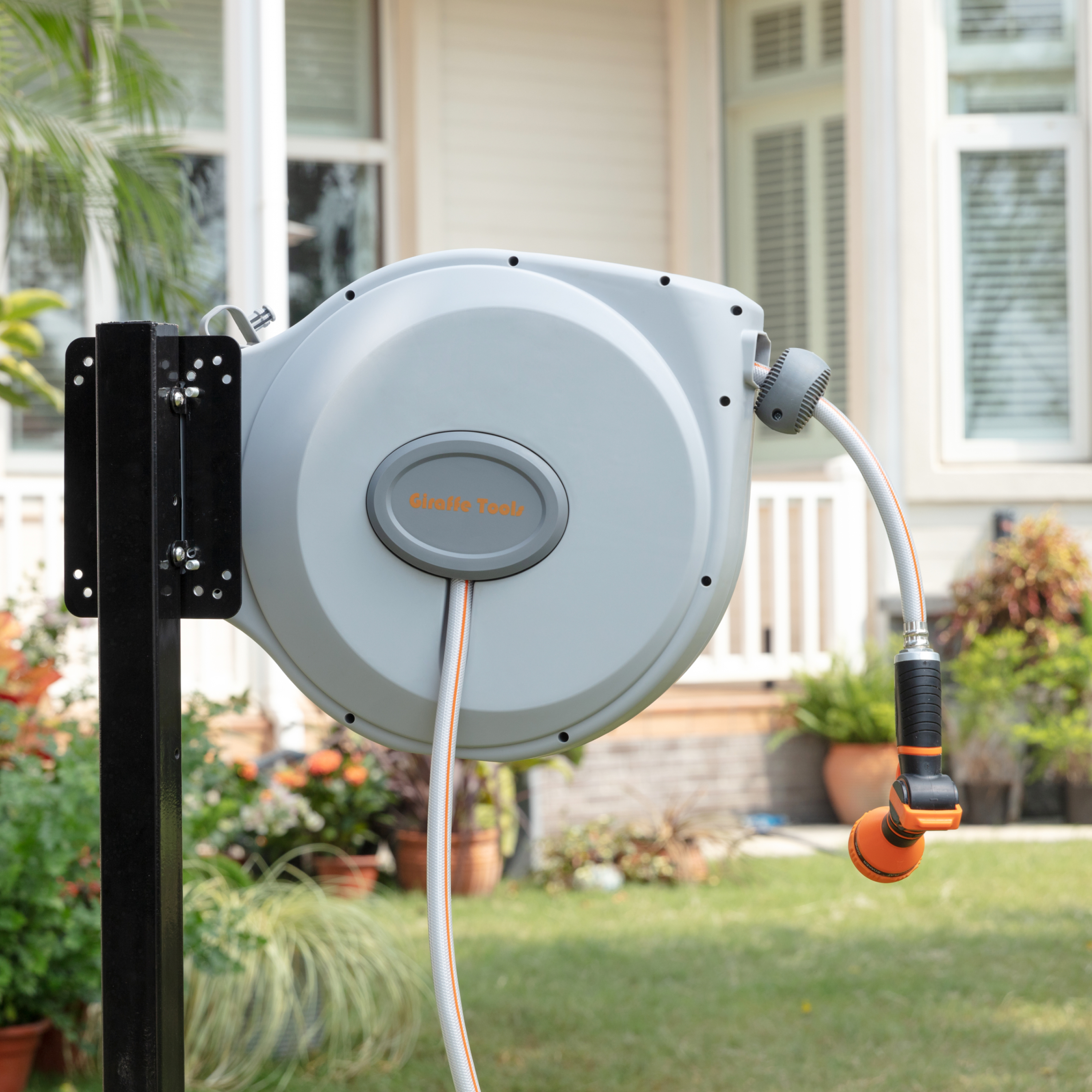 Wall-mounted retractable hose reel in light gray with connected inlet hose and nozzle
