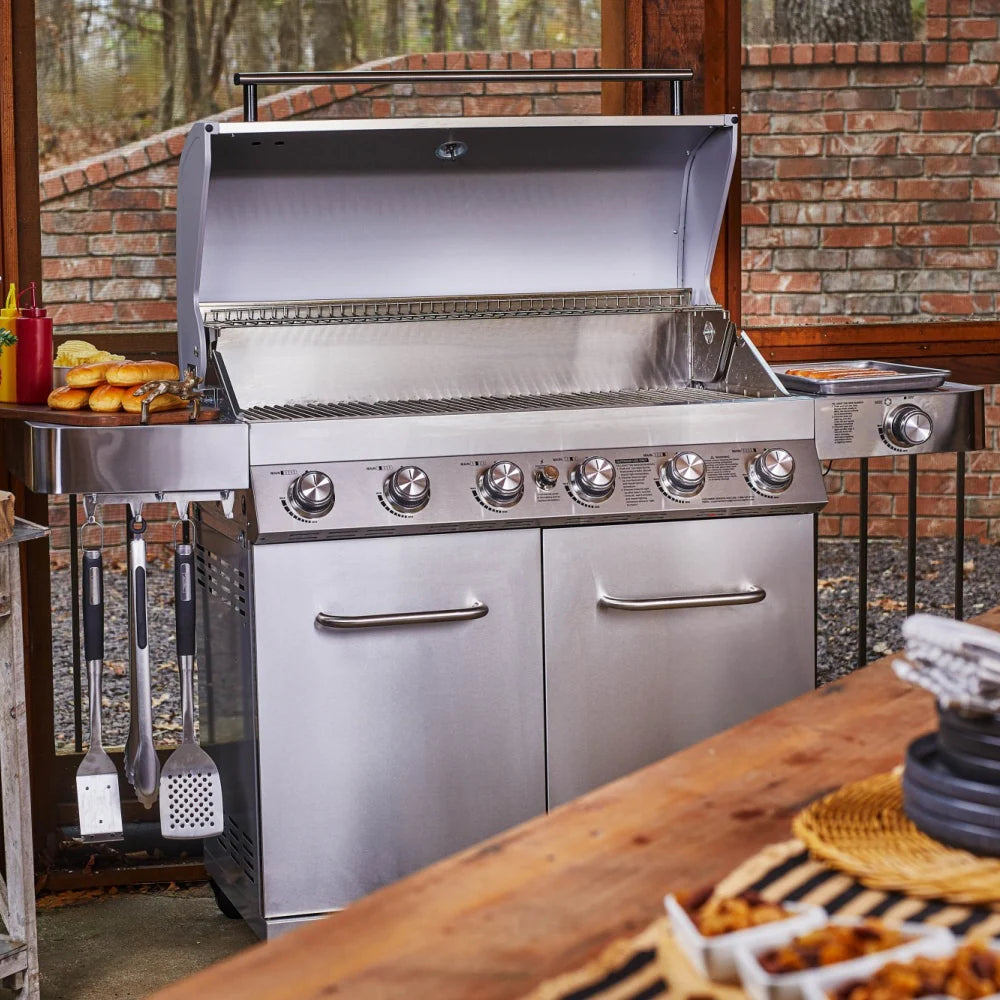 Stainless steel gas grill with open lid, six burner knobs, and storage doors