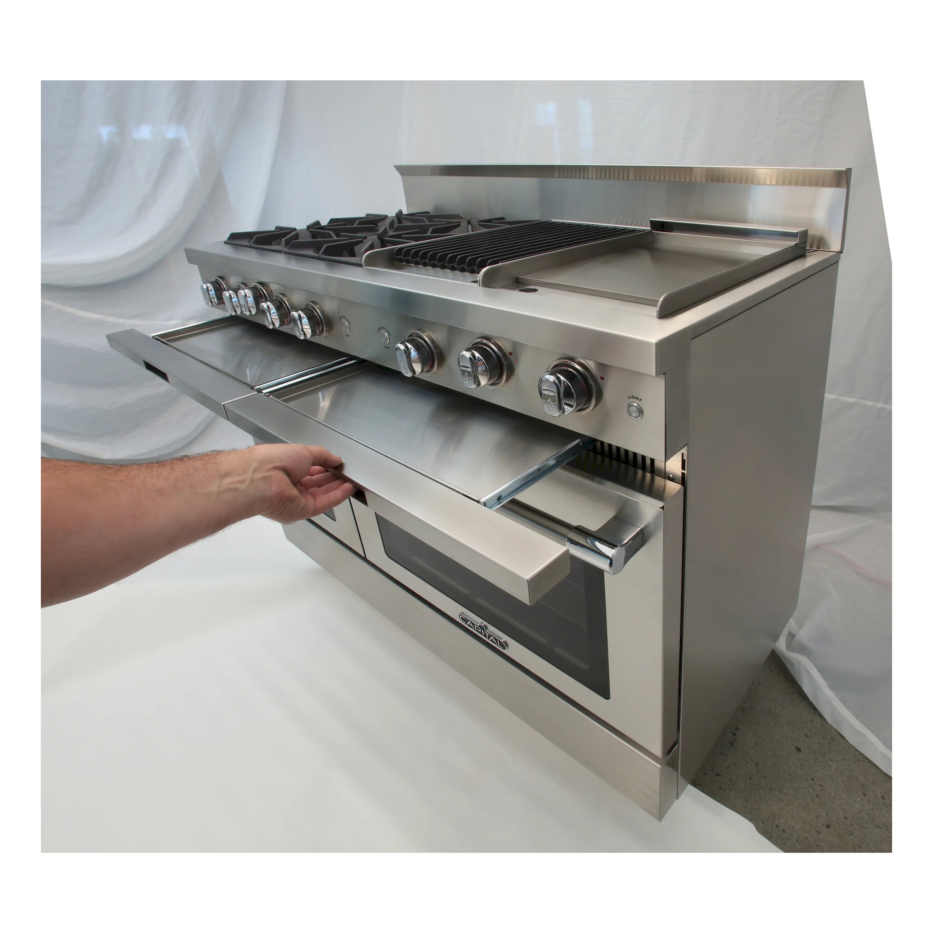 Hand pulling out griddle drawer on stainless steel gas range, oven door closed