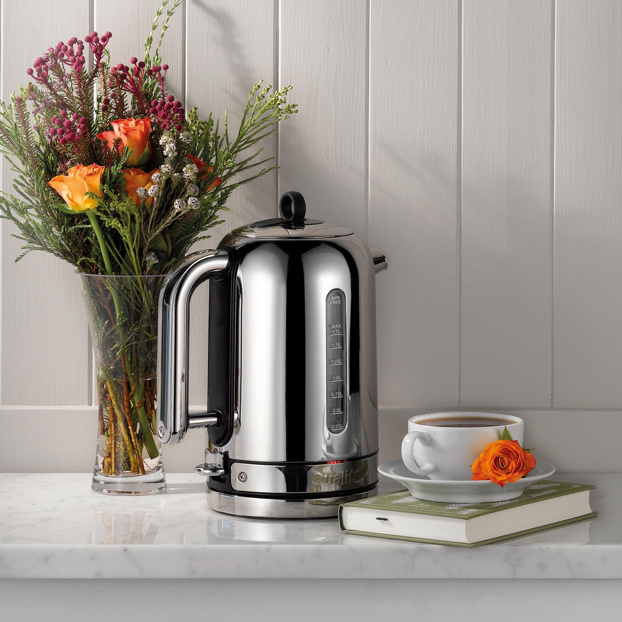 Polished chrome electric kettle on kitchen counter beside floral arrangement and cup.