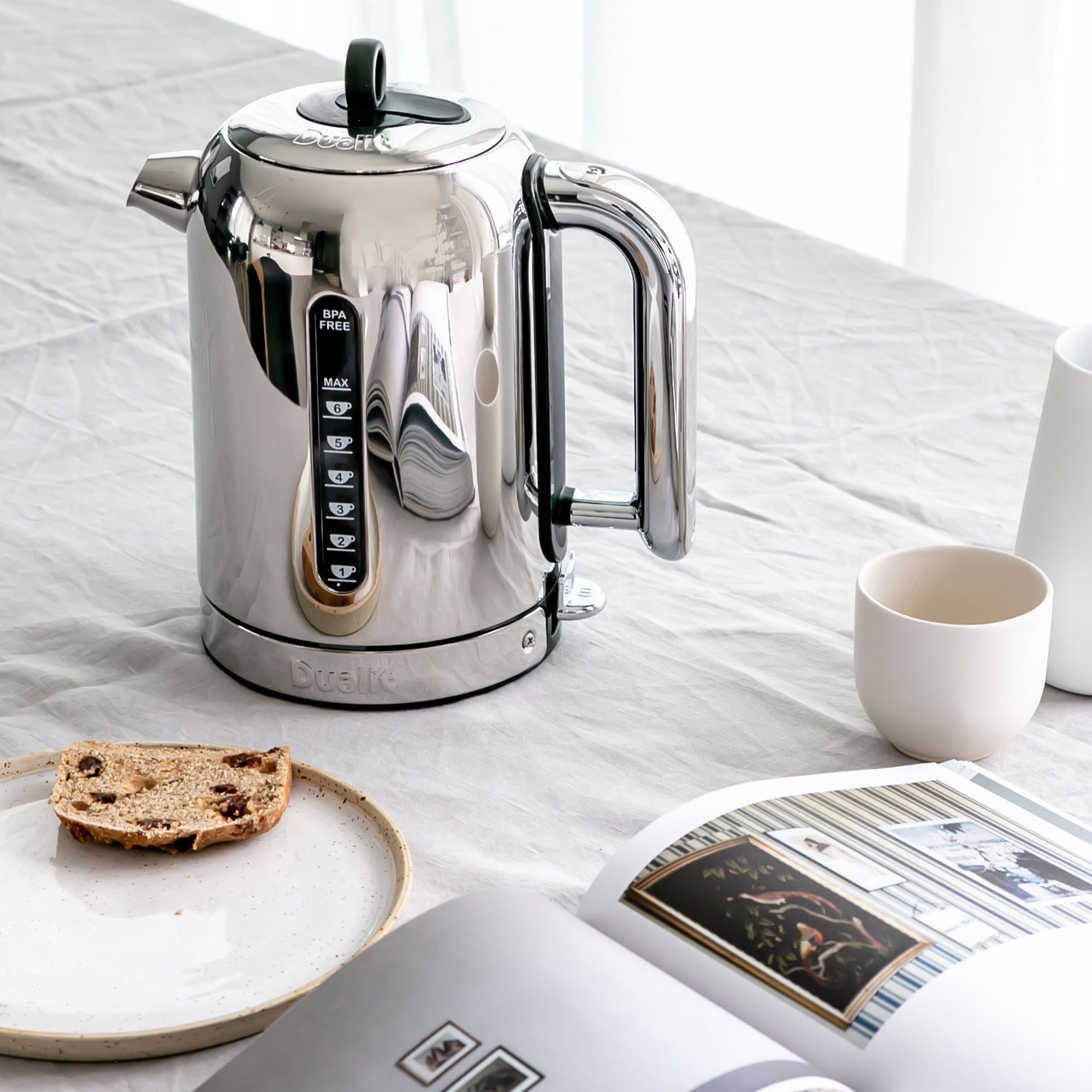Dualit polished chrome electric kettle with black lid, spout, and control base on counter.