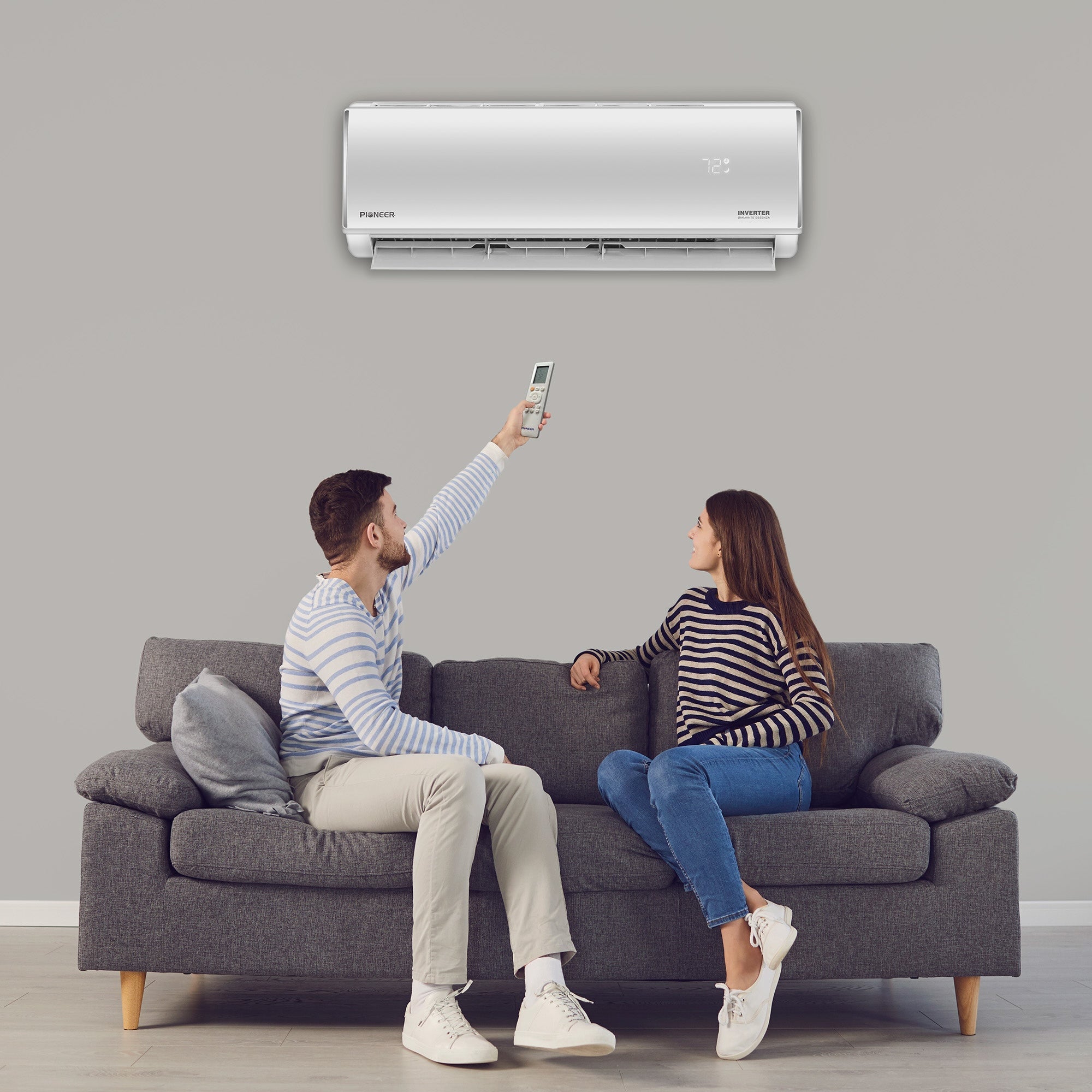 White ductless mini-split wall unit above living-room sofa with two people seated