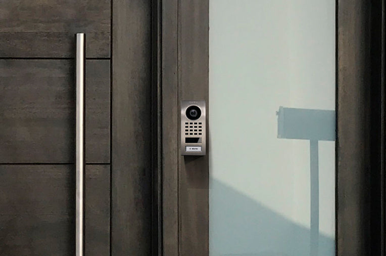 DoorBird surface-mount video intercom on exterior door frame with camera and keypad