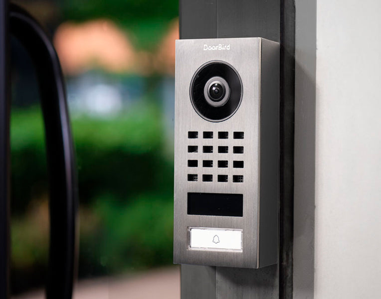 DoorBird surface-mount IP video intercom with camera, keypad grid, and doorbell button.