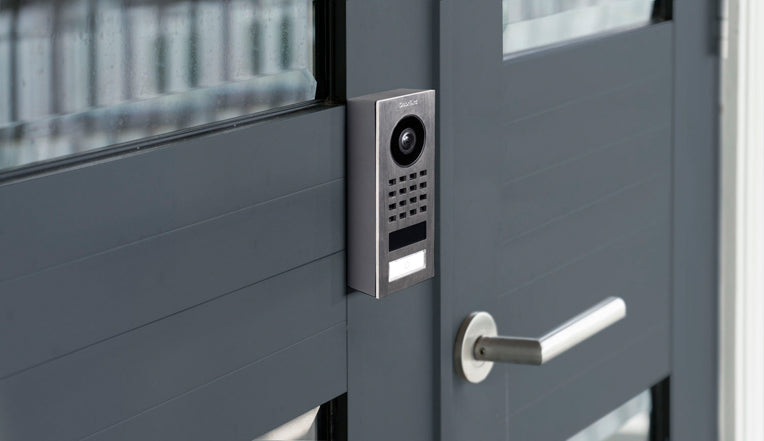 DoorBird surface-mount video intercom on entry door with camera and keypad