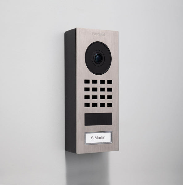 Grey metal surface-mount video intercom panel with round camera, keypad grid, label area