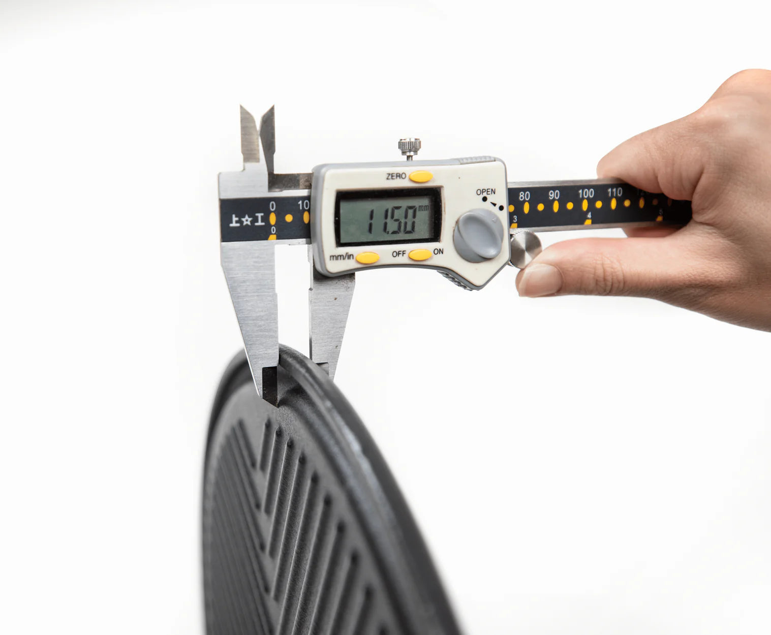 Round cast iron cooking plate measured with a digital caliper showing thickness