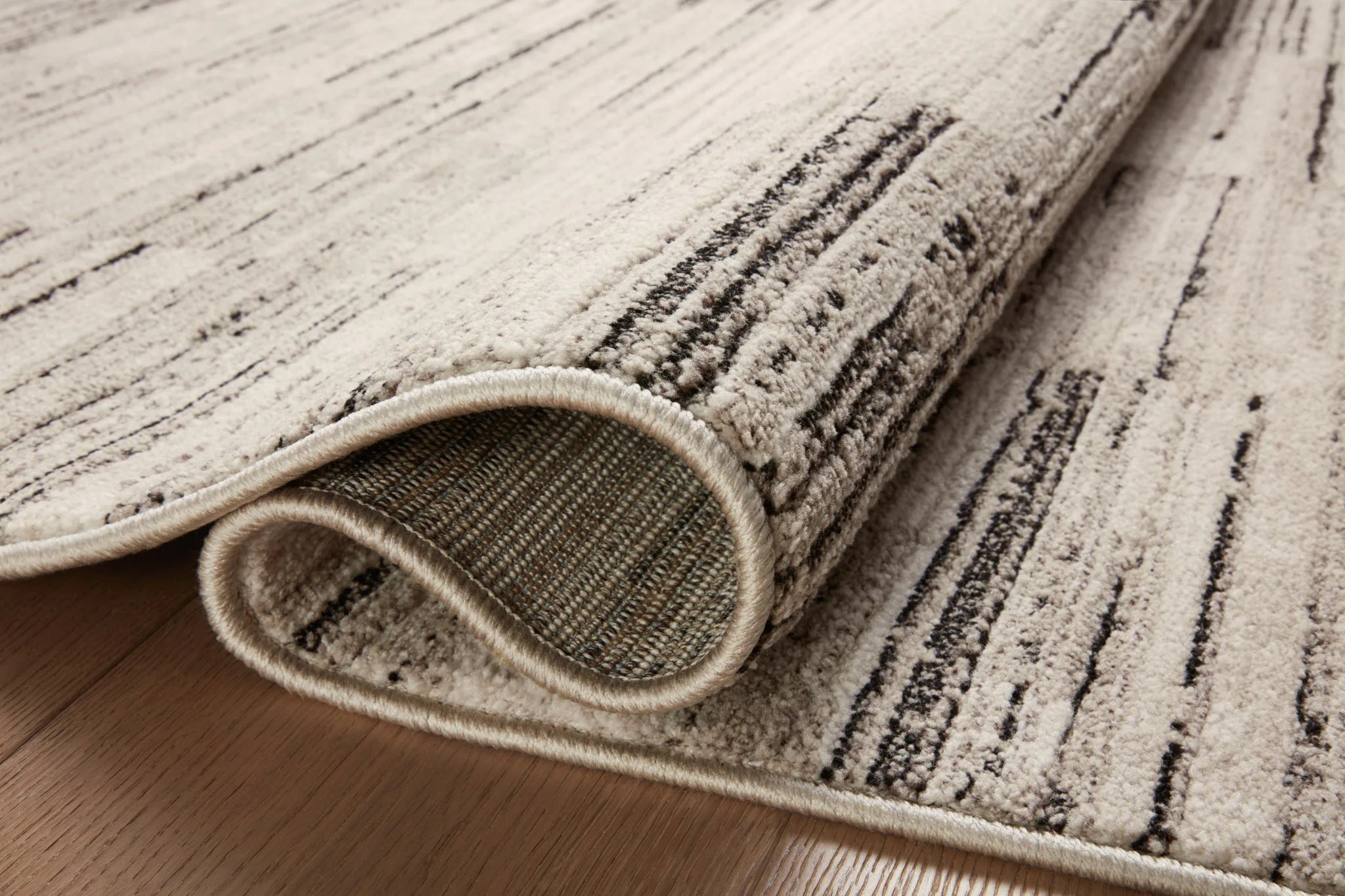 Charcoal and sand area rug corner detail with rolled edge and stitched fabric border