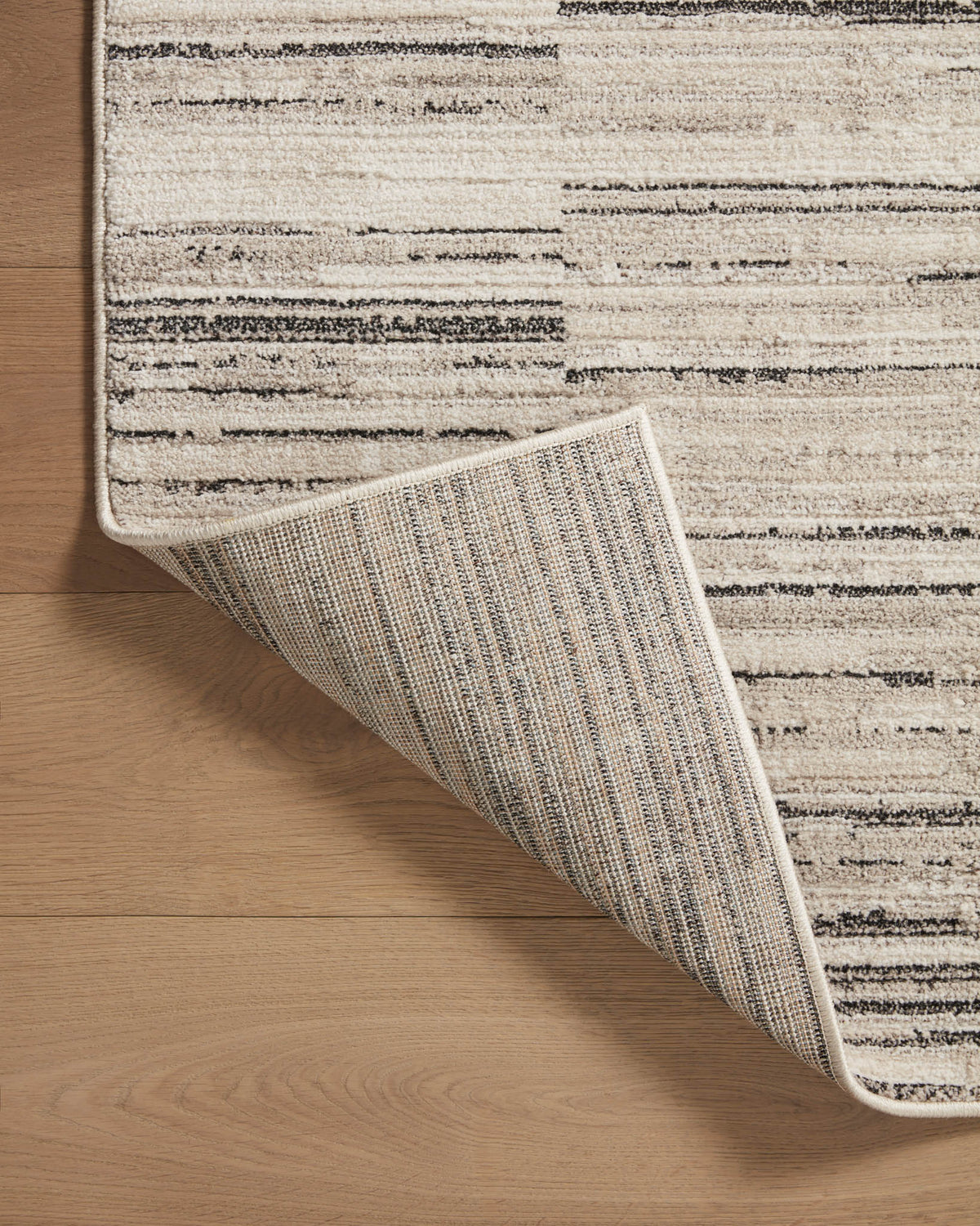 Charcoal and sand area rug corner with visible woven backing and bound edge
