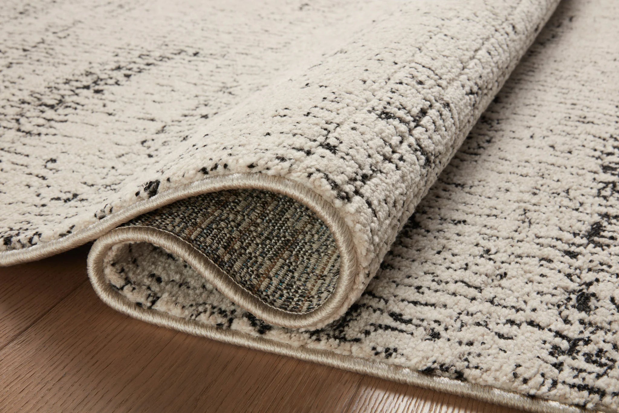 Accent rug corner with bound edge showing oatmeal and charcoal textured pile