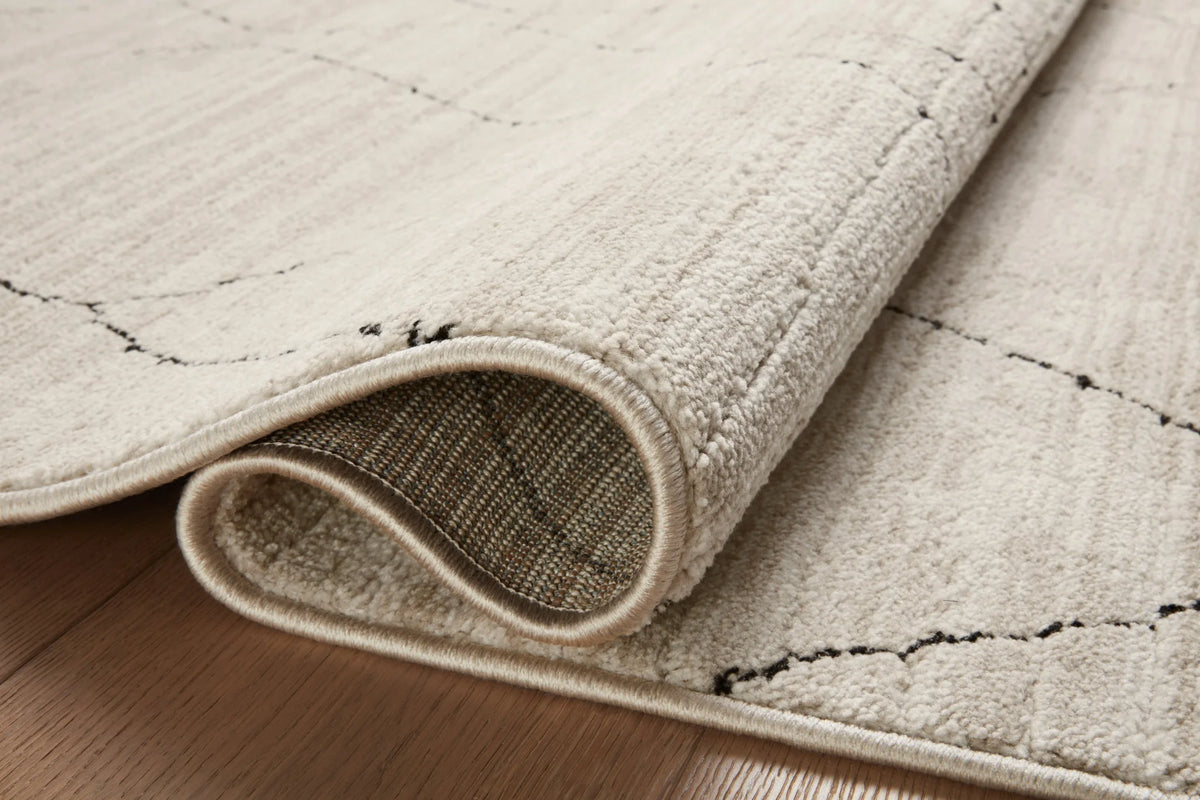 Rolled edge detail of sand area rug with charcoal diamond line pattern